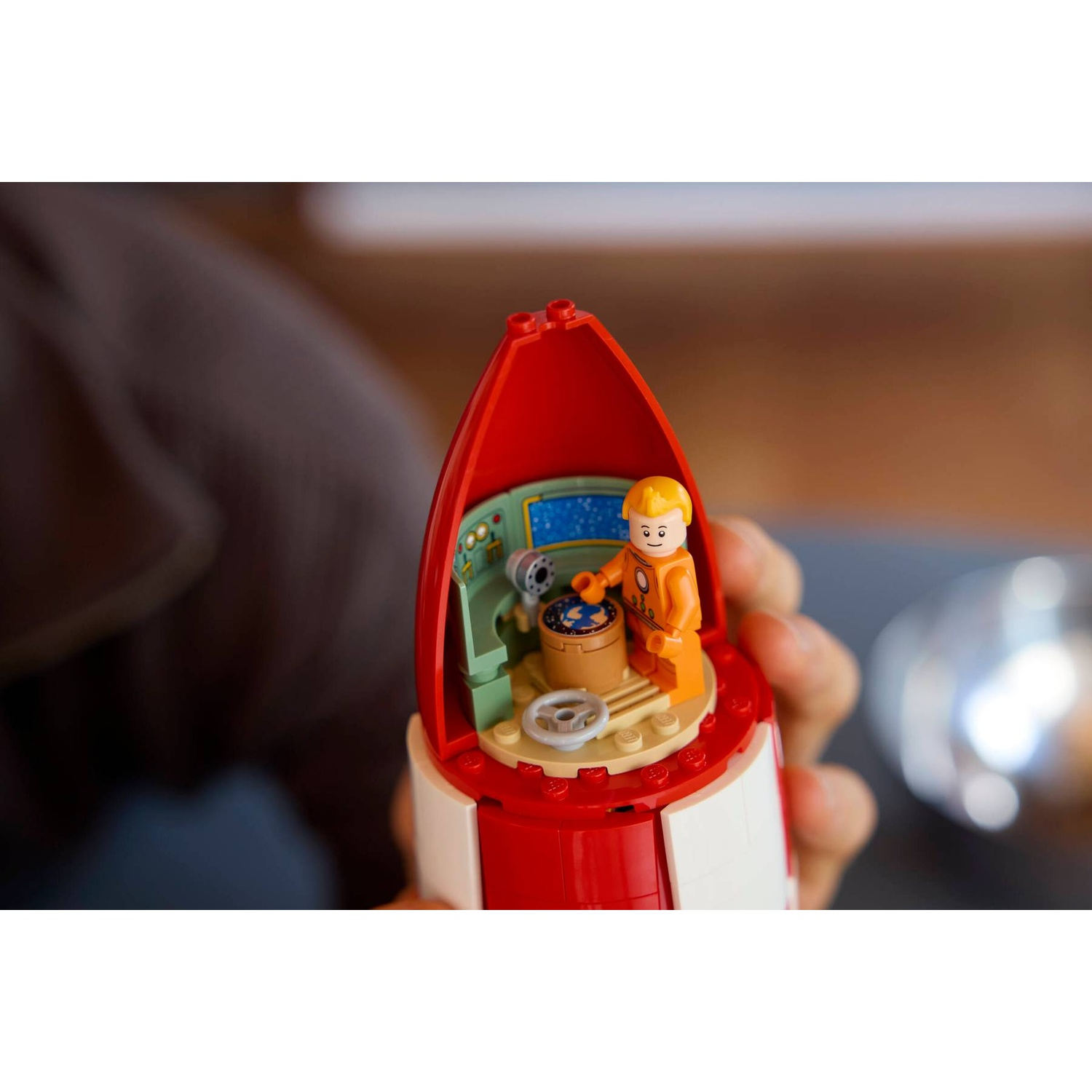 A Lego astronaut in a red rocket cockpit with controls.