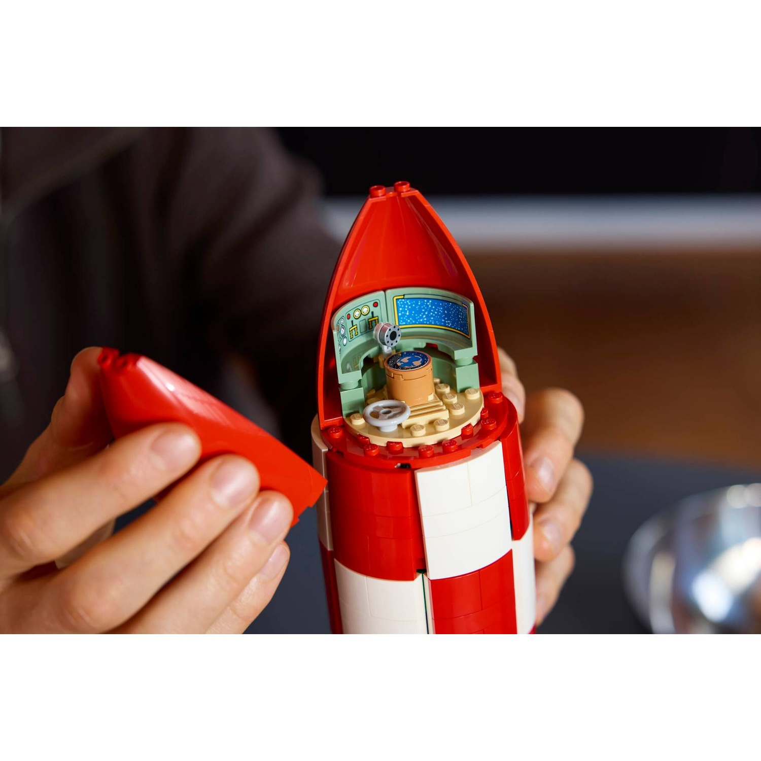 Person building red and white Lego rocket with detailed cockpit inside.
