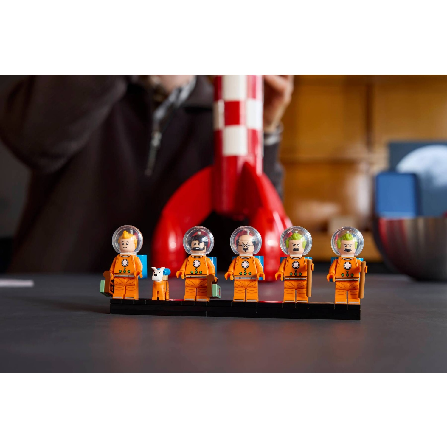 Five Lego astronauts and a dog stand before a red and white rocket.