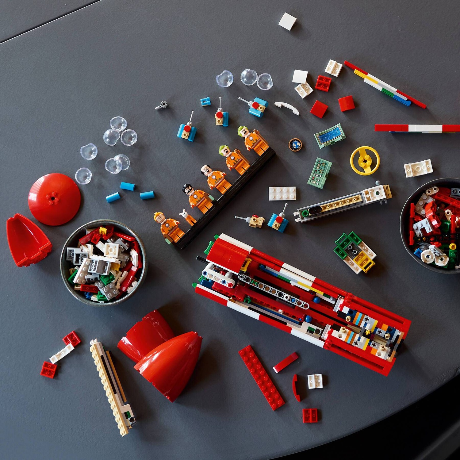 Lego building blocks and figures, including astronauts, a rocket, and accessories, are scattered on a gray surface.