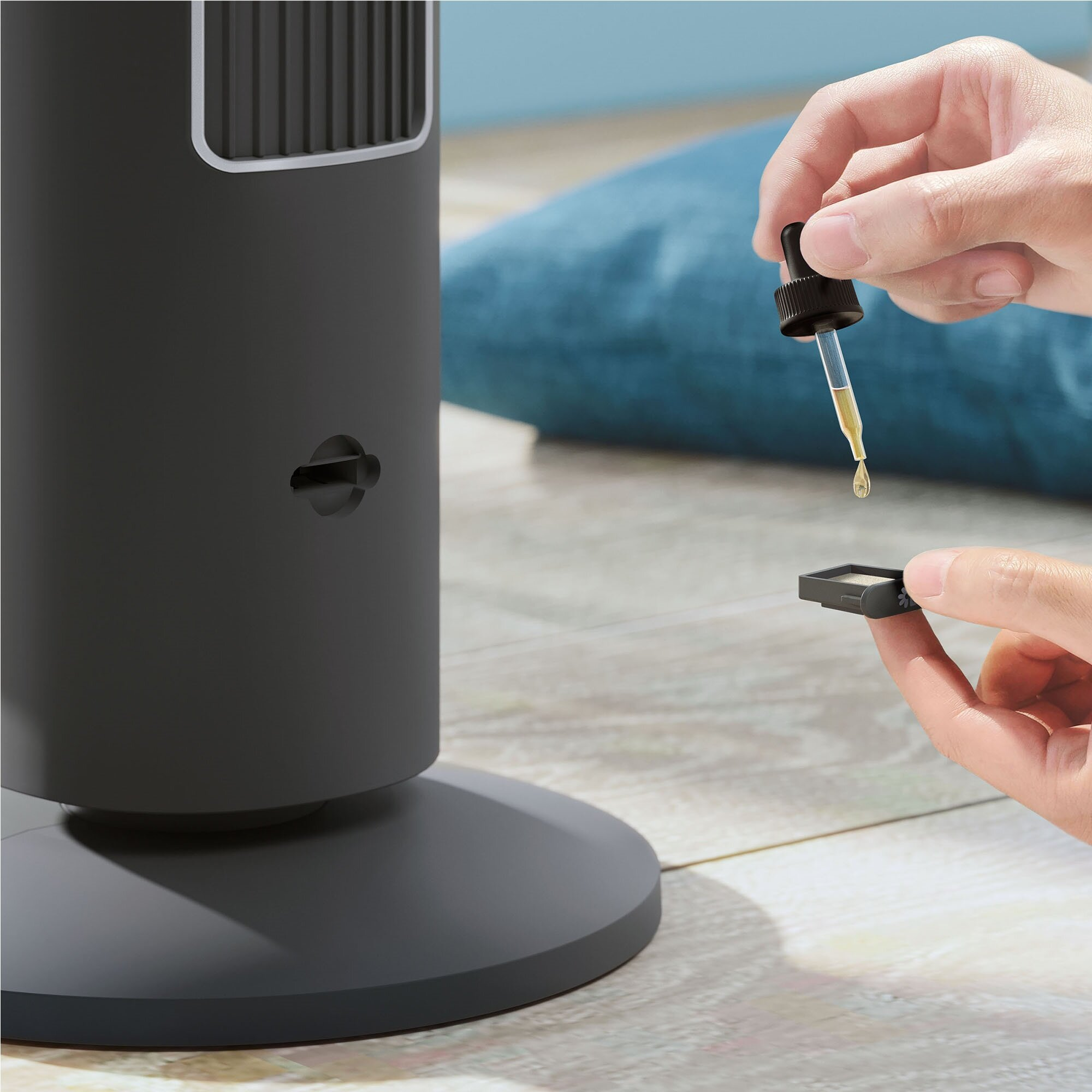 Dłoń trzyma zakraplacz z płynem, kapie na mały filtr obok czarnego wentylatora.