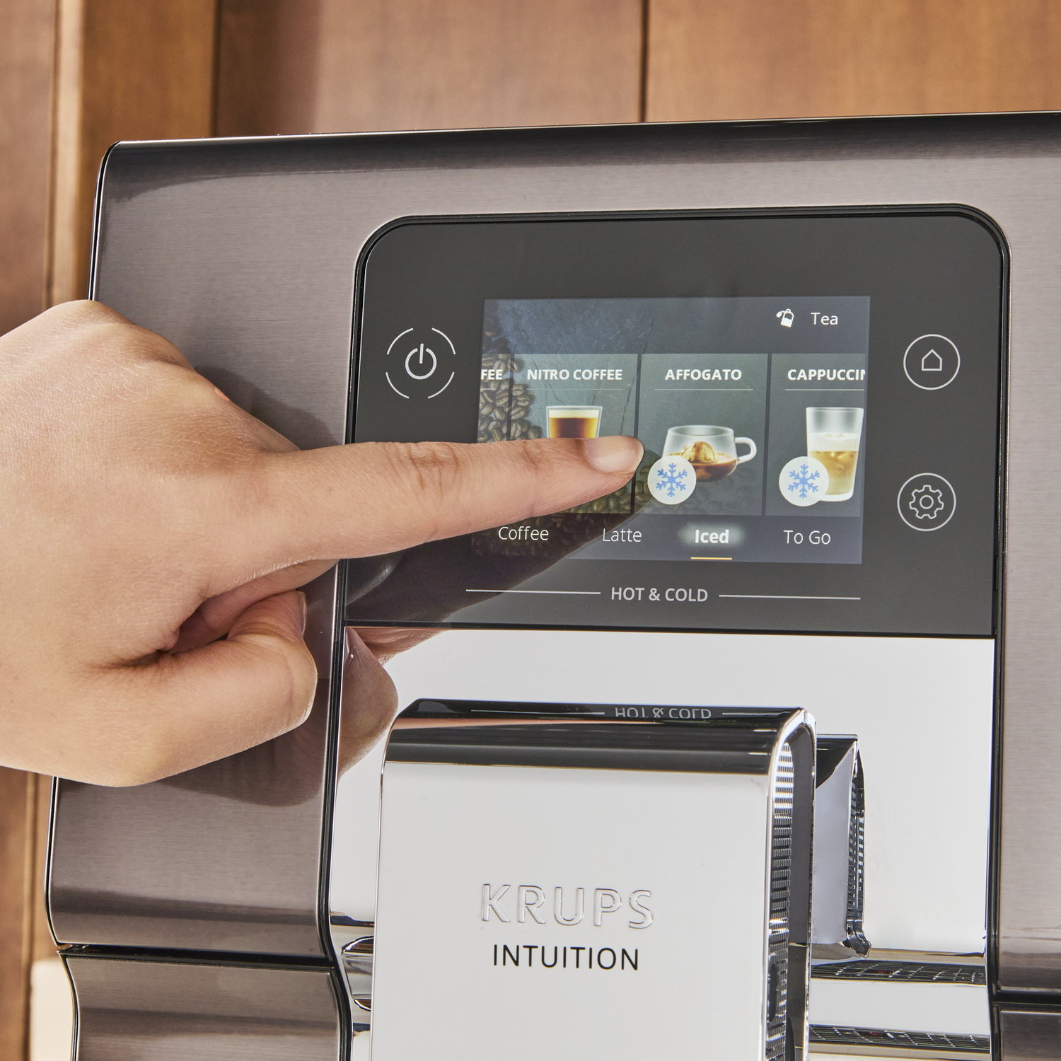 Een hand raakt een koffiemachine-scherm aan met drankopties.