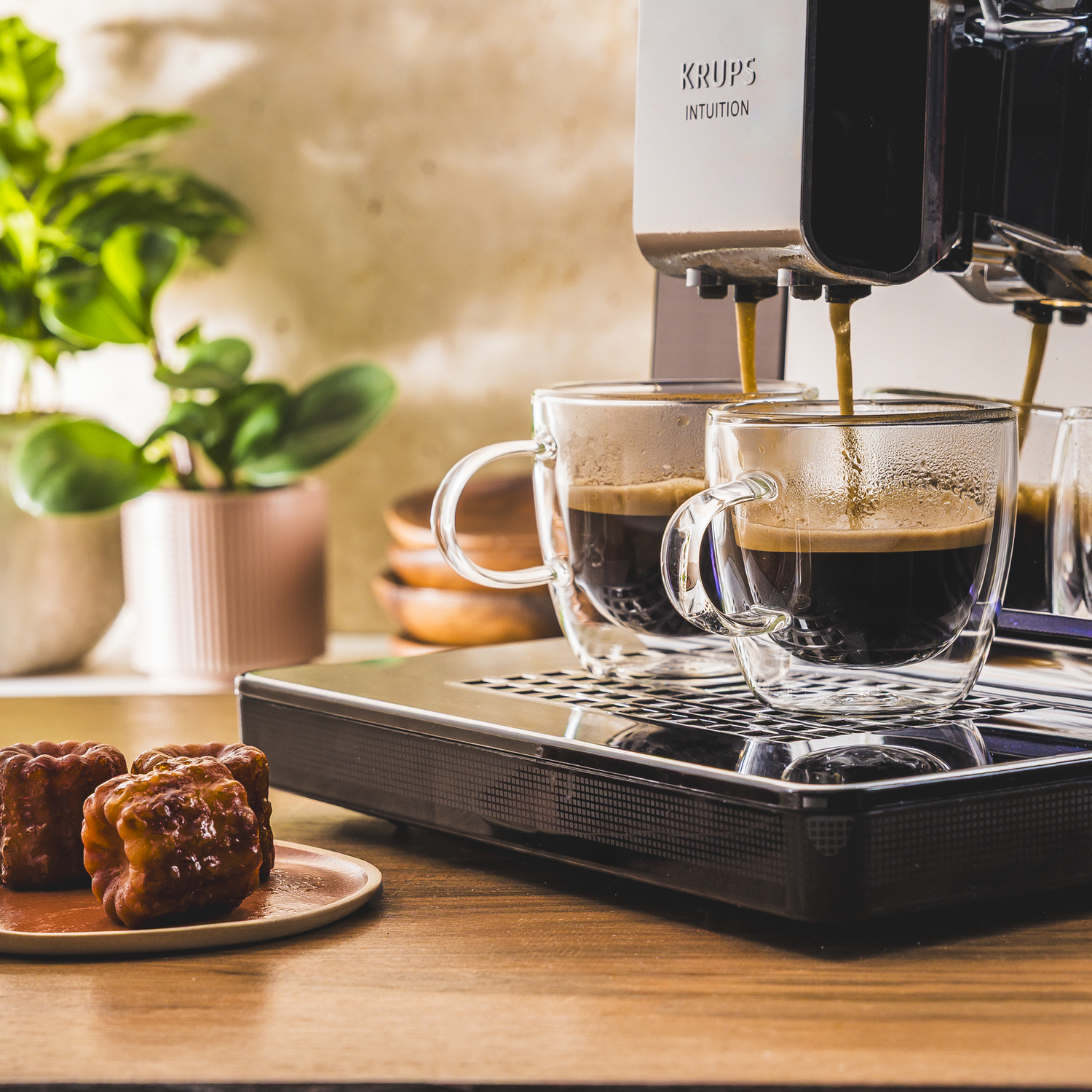 Koffiezetapparaat zet espresso in twee glazen, canelés op een bord.