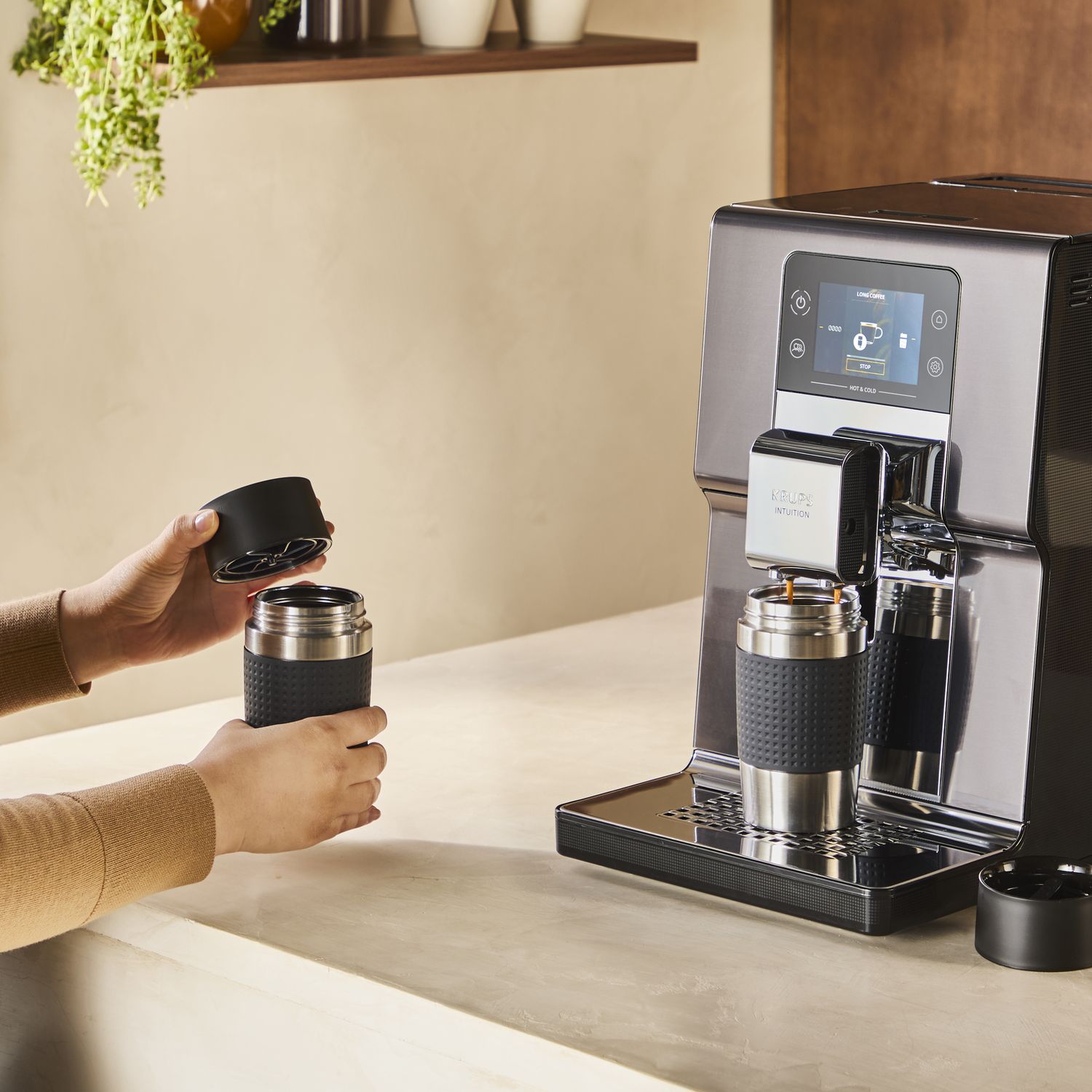 Een koffiezetapparaat zet koffie in een reismok die door een persoon wordt vastgehouden.