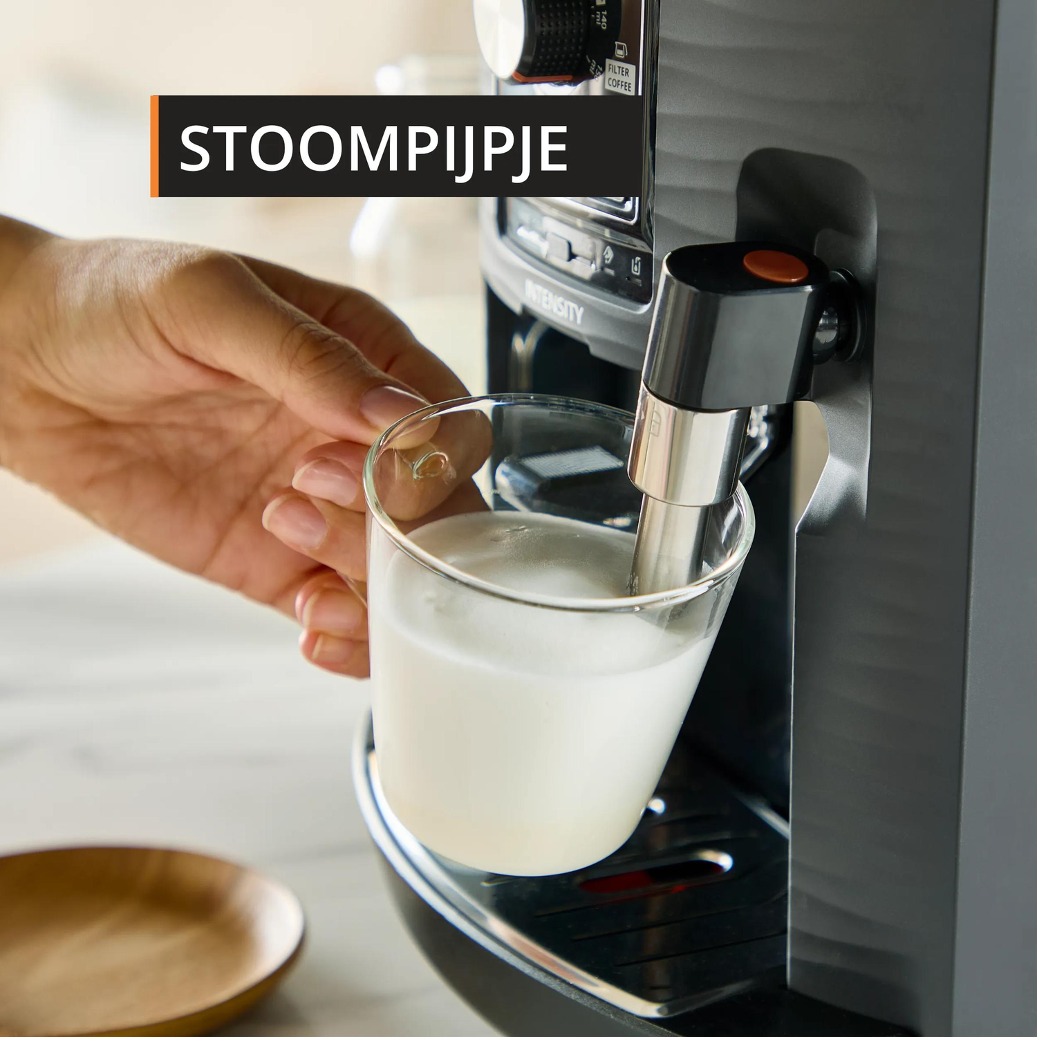 A hand holds a glass of white liquid as a coffee machine froths milk.