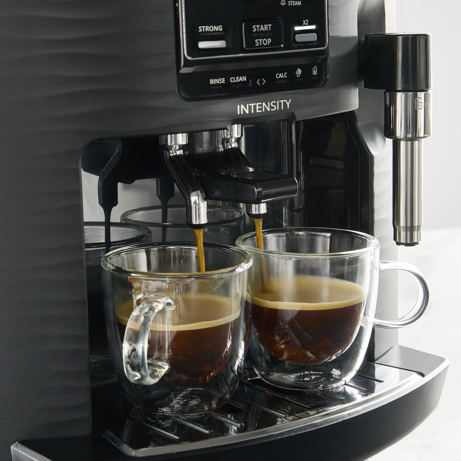 Espresso pouring into two clear glass mugs from a black coffee machine.
