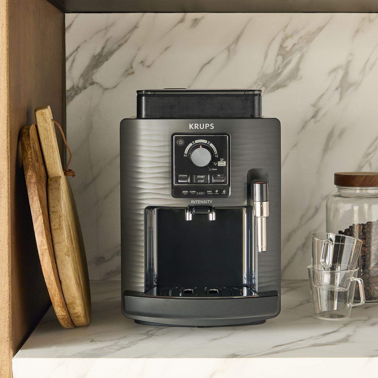 A grey Krups coffee machine with controls sits on a marble counter with coffee beans.