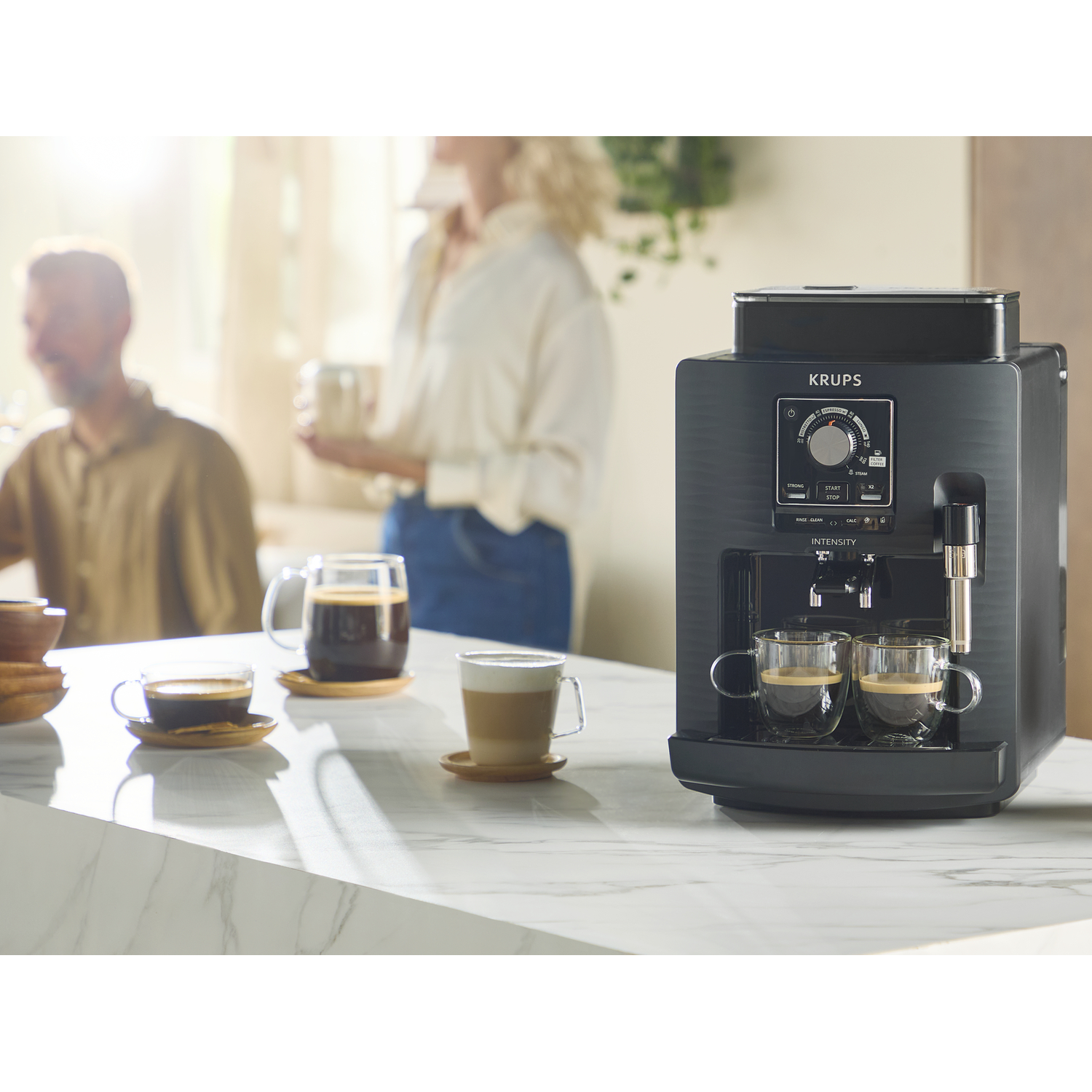 A Krups coffee machine brews two espressos into glass cups on a marble countertop.