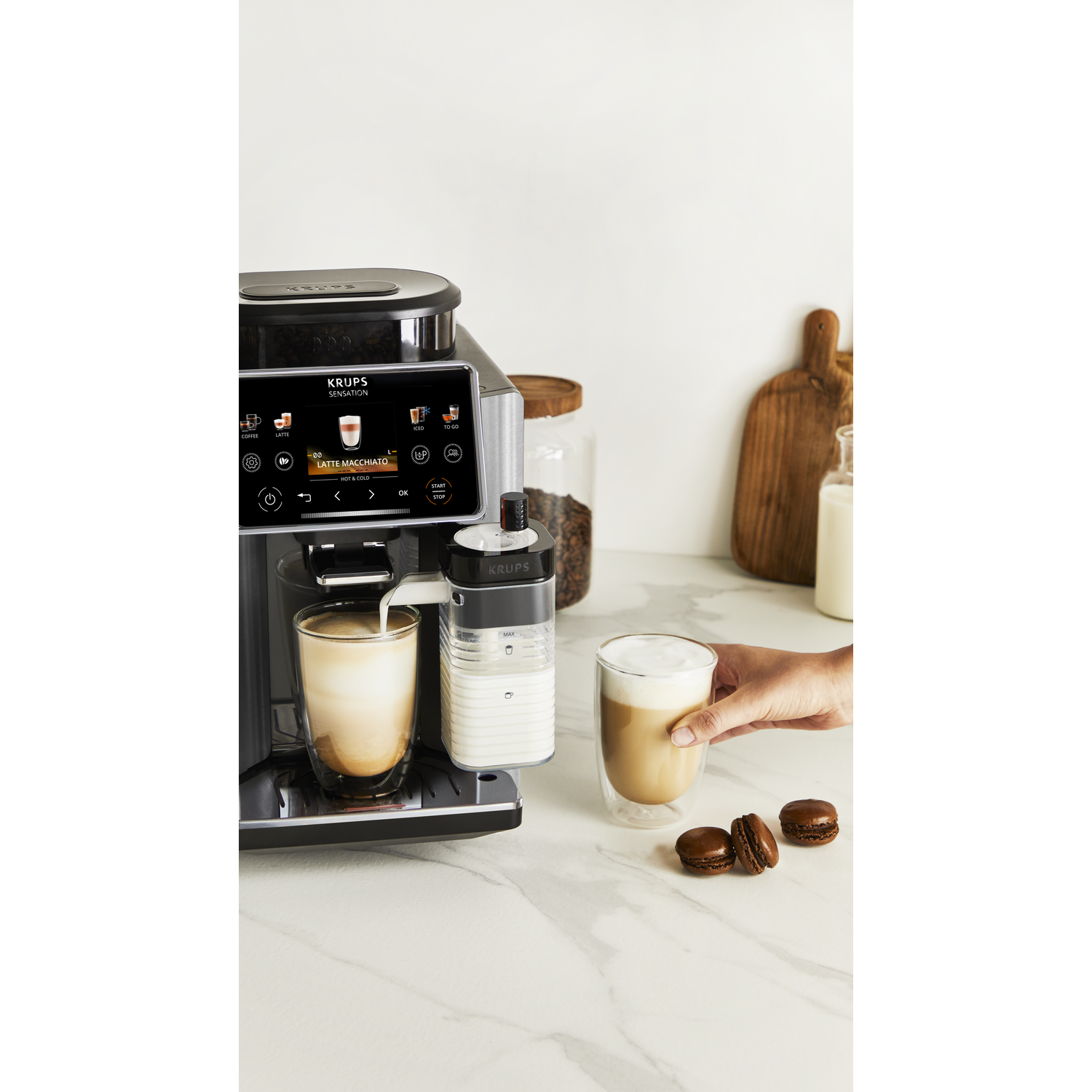 Een Krups koffiezetapparaat maakt een latte macchiato in een doorzichtig glas.