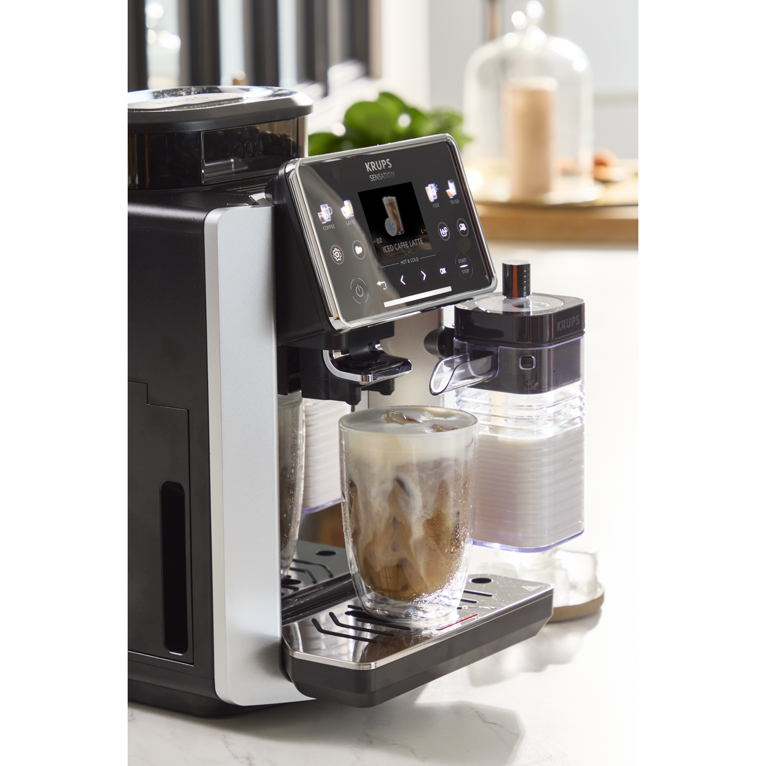 Een zwart-zilveren Krups koffiezetapparaat maakt een ijsthee latte in een glas.