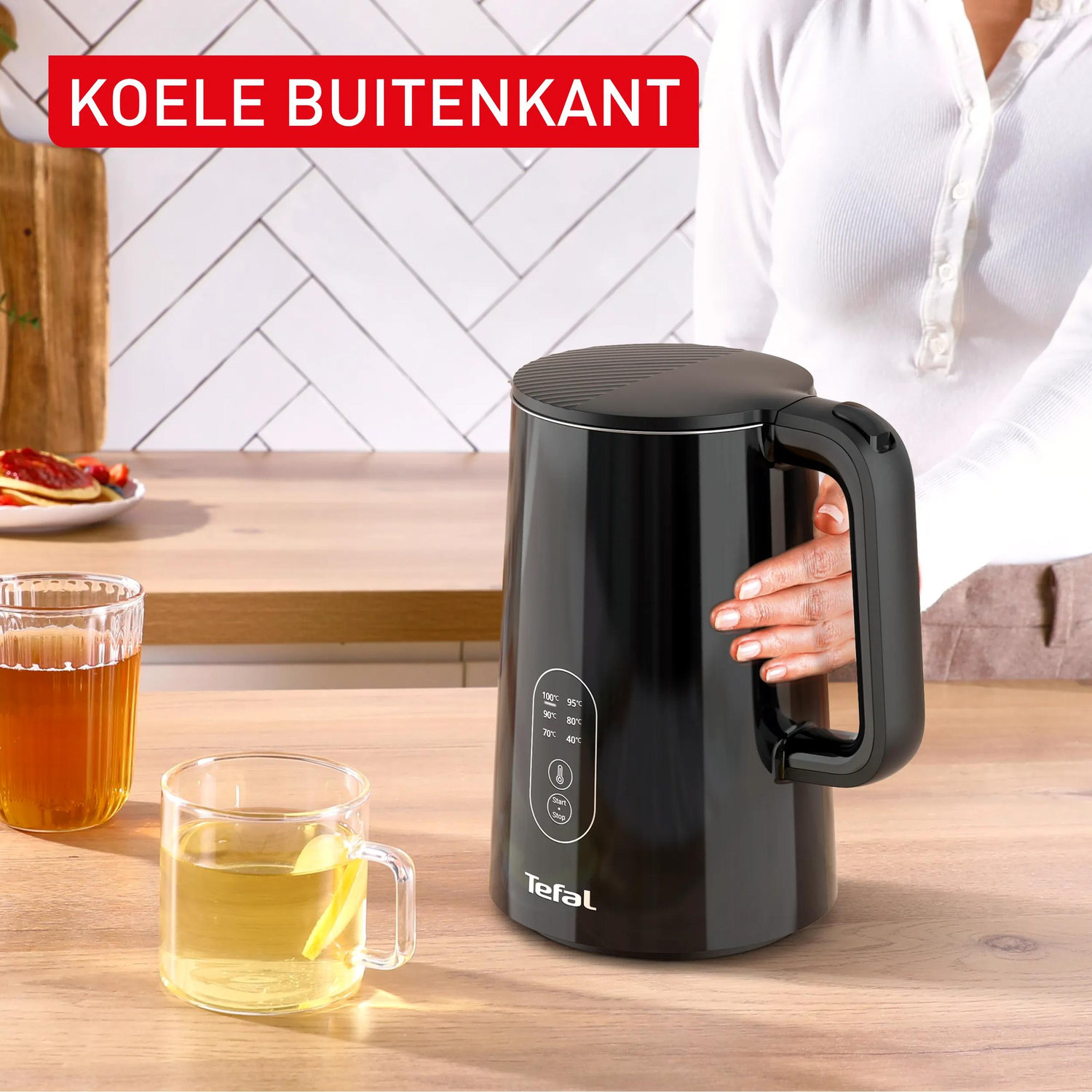 Zwarte waterkoker met handvat, naast twee glazen met drankjes.