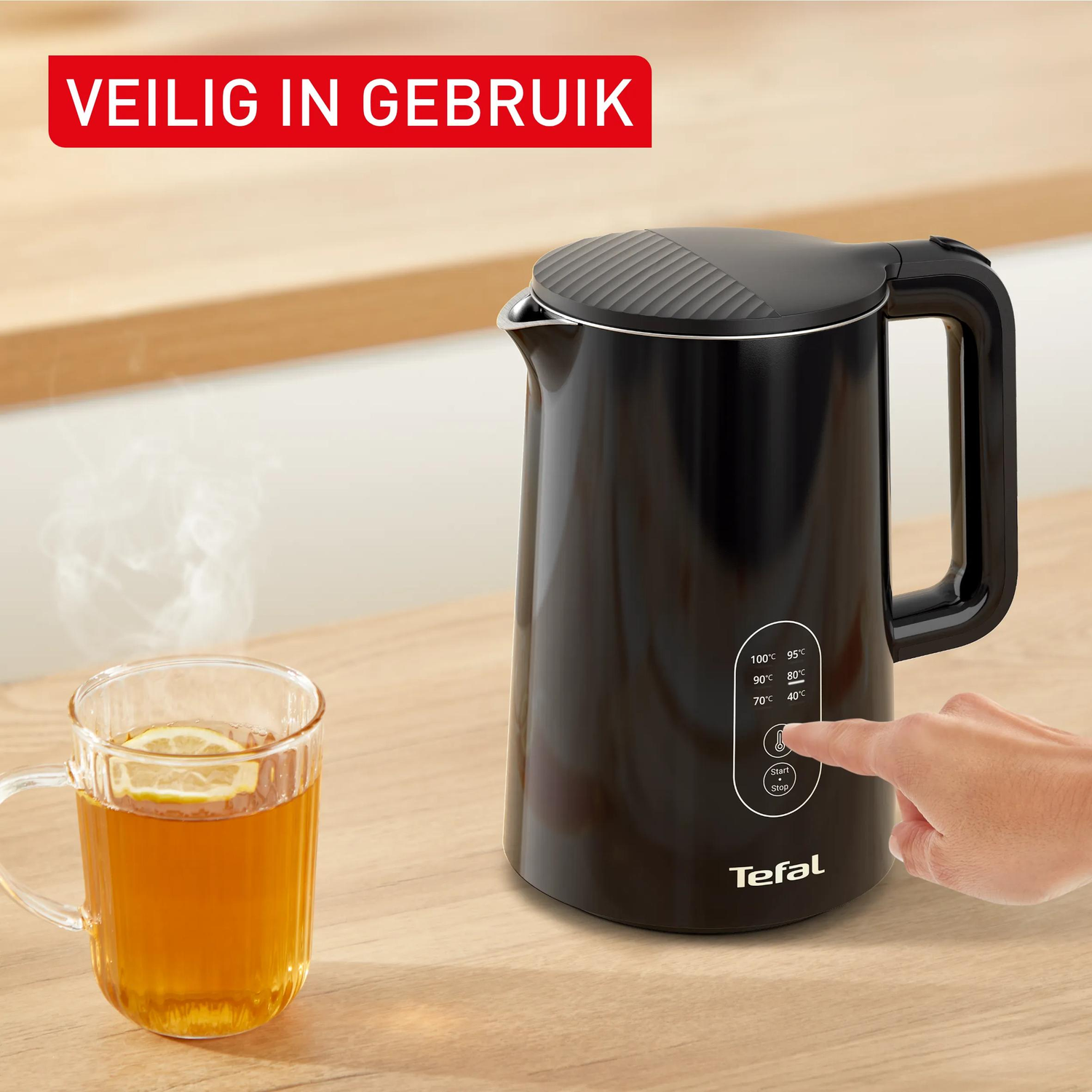 Zwarte waterkoker met temperatuurweergave en dampende kop thee op houten tafel.