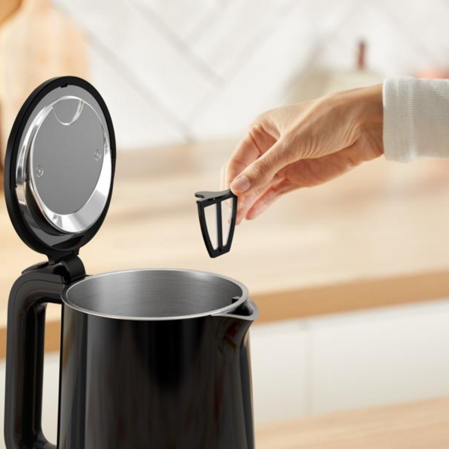 Een hand plaatst een zwart filter in een open zwarte waterkoker.