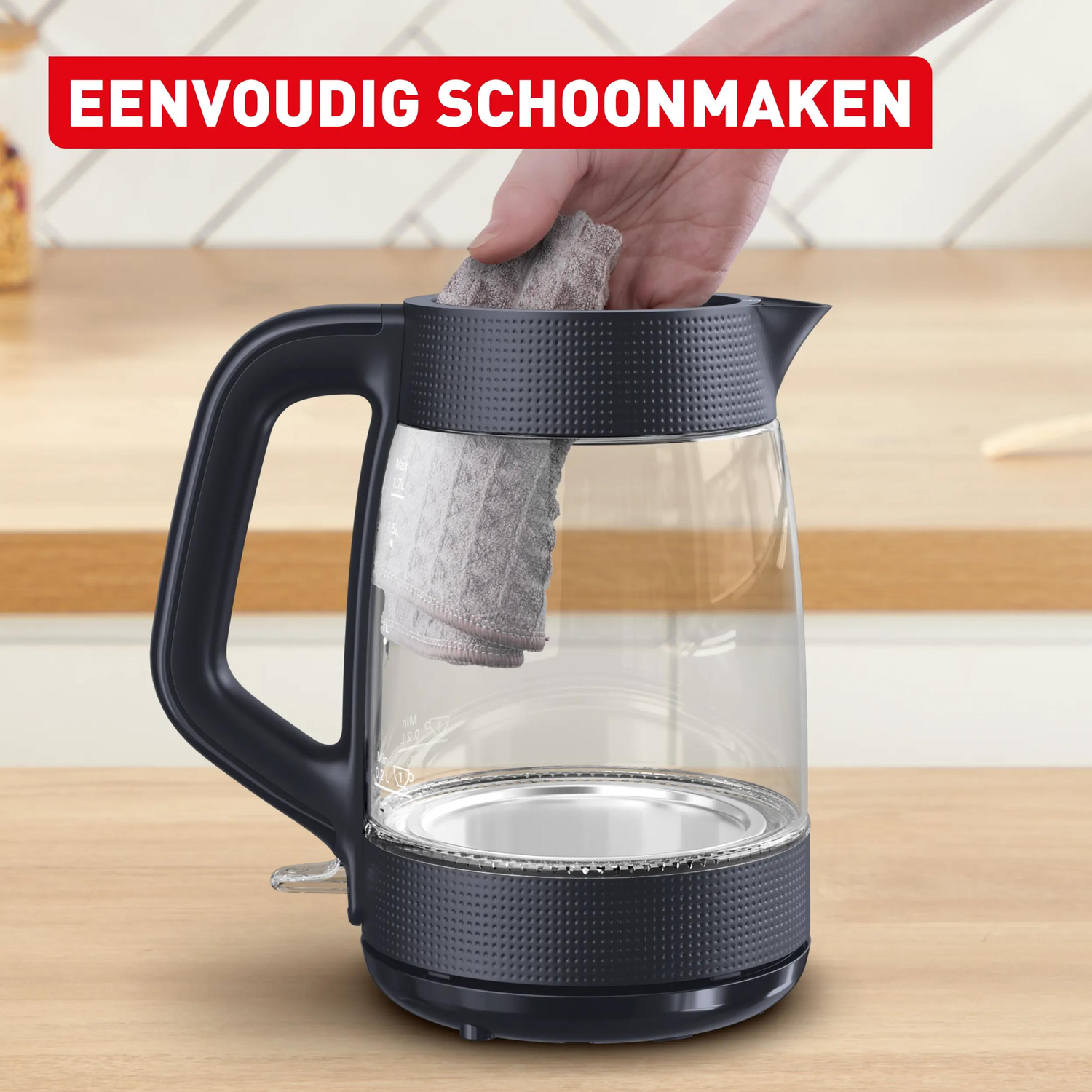 Een hand maakt een glazen waterkoker schoon met een grijze doek.