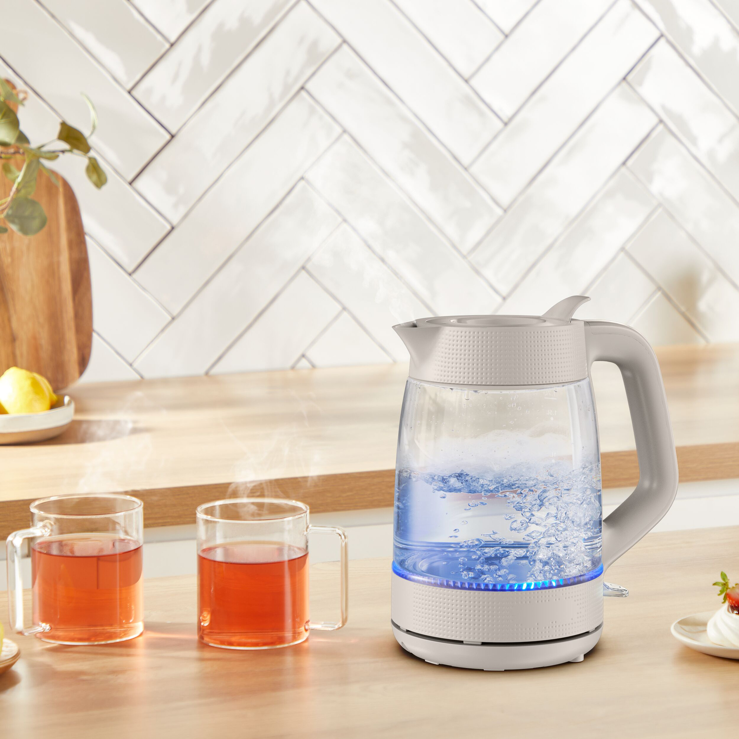 A kettle boils water on a wooden counter next to two cups of tea.