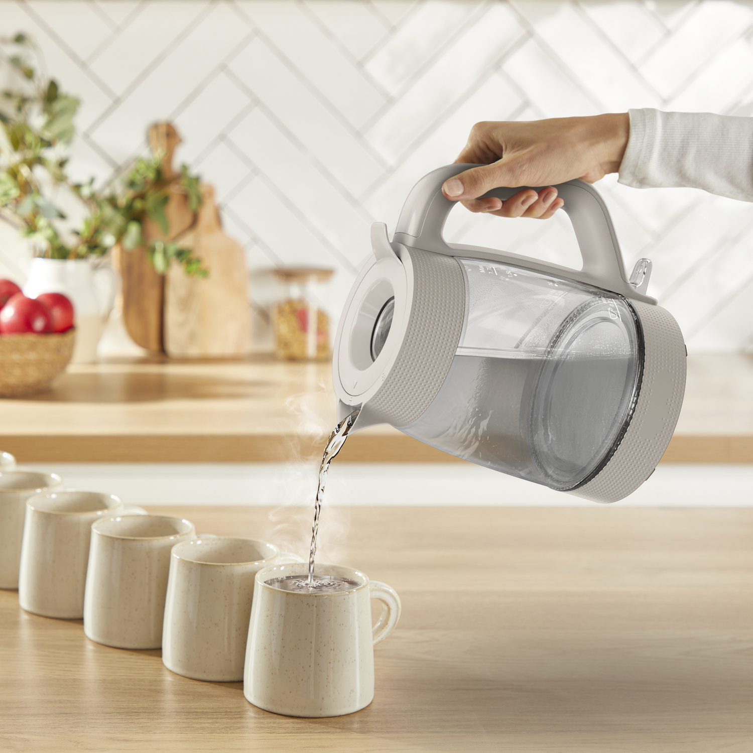 A hand pours hot water from a kettle into a row of mugs on a wooden counter.