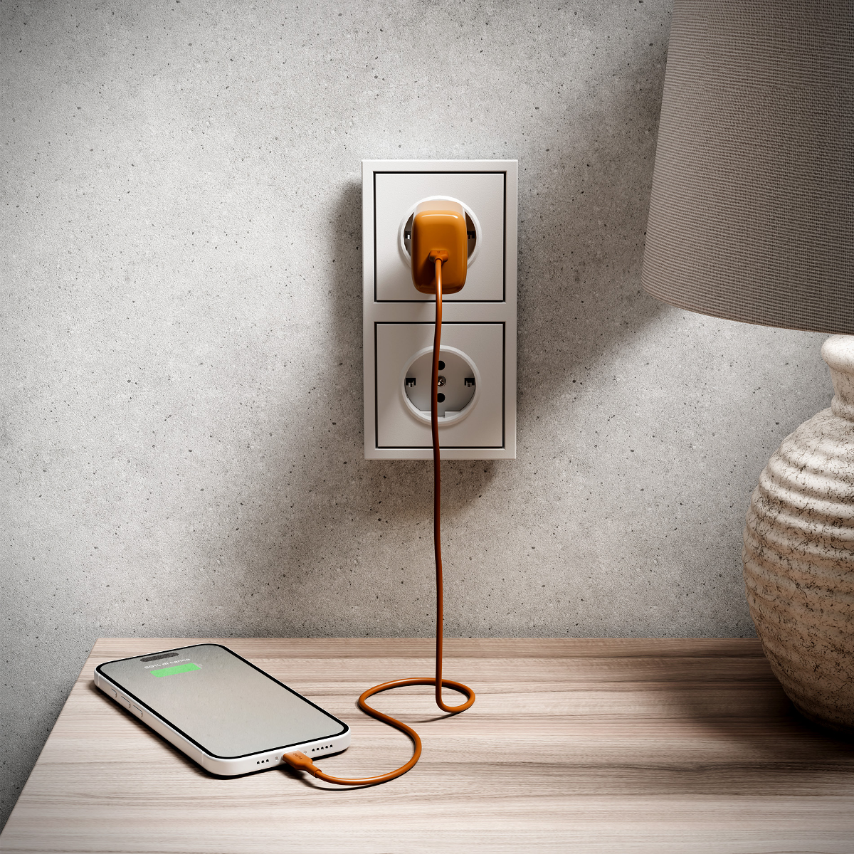 Ein Smartphone wird über ein orangefarbenes Kabel an eine Wandsteckdose geladen.