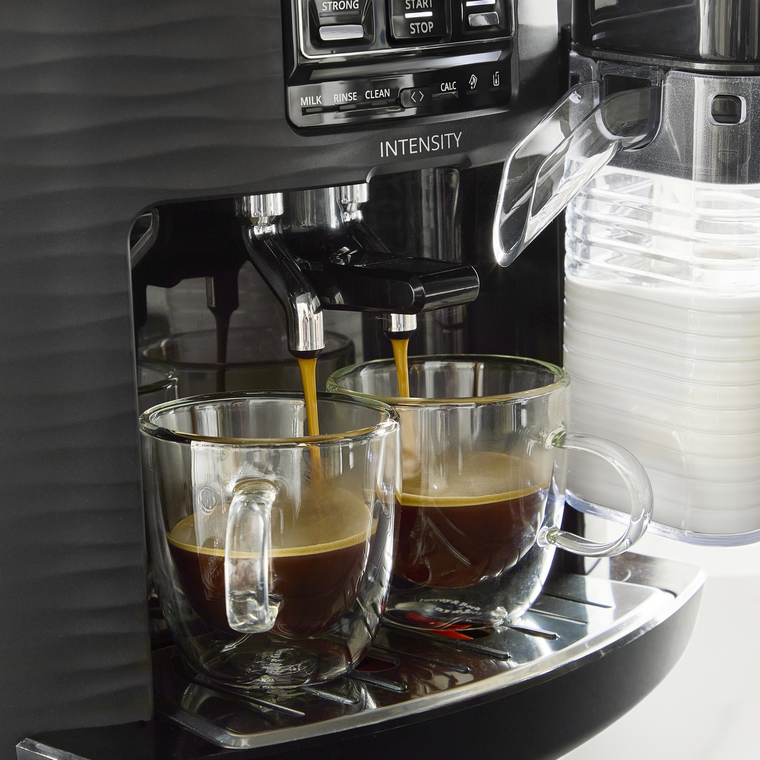 Espresso pours into two clear glass cups from a black coffee machine.