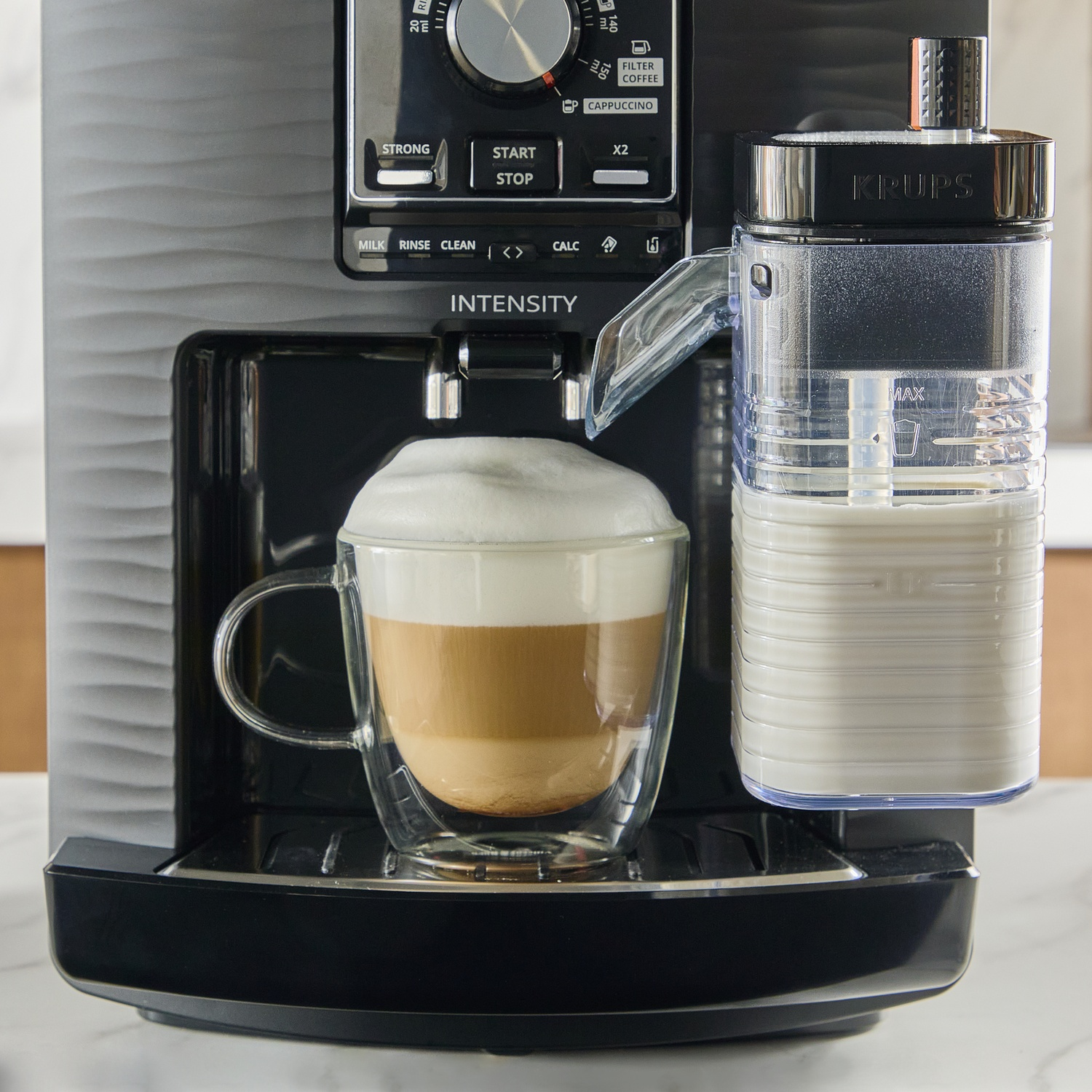 Coffee machine with frothed milk in a glass and milk tank beside it.