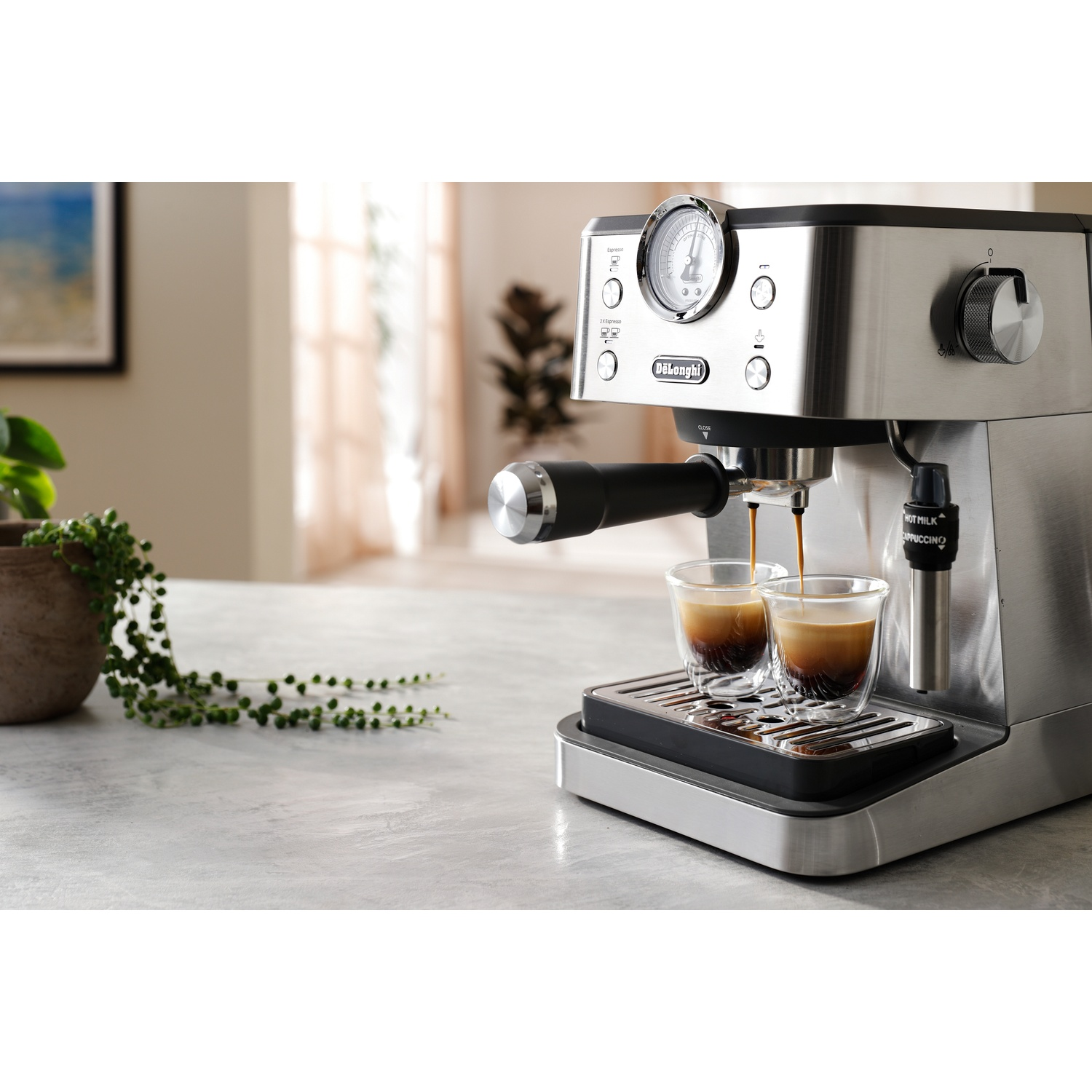 A silver espresso machine brews coffee into two glasses on a table.