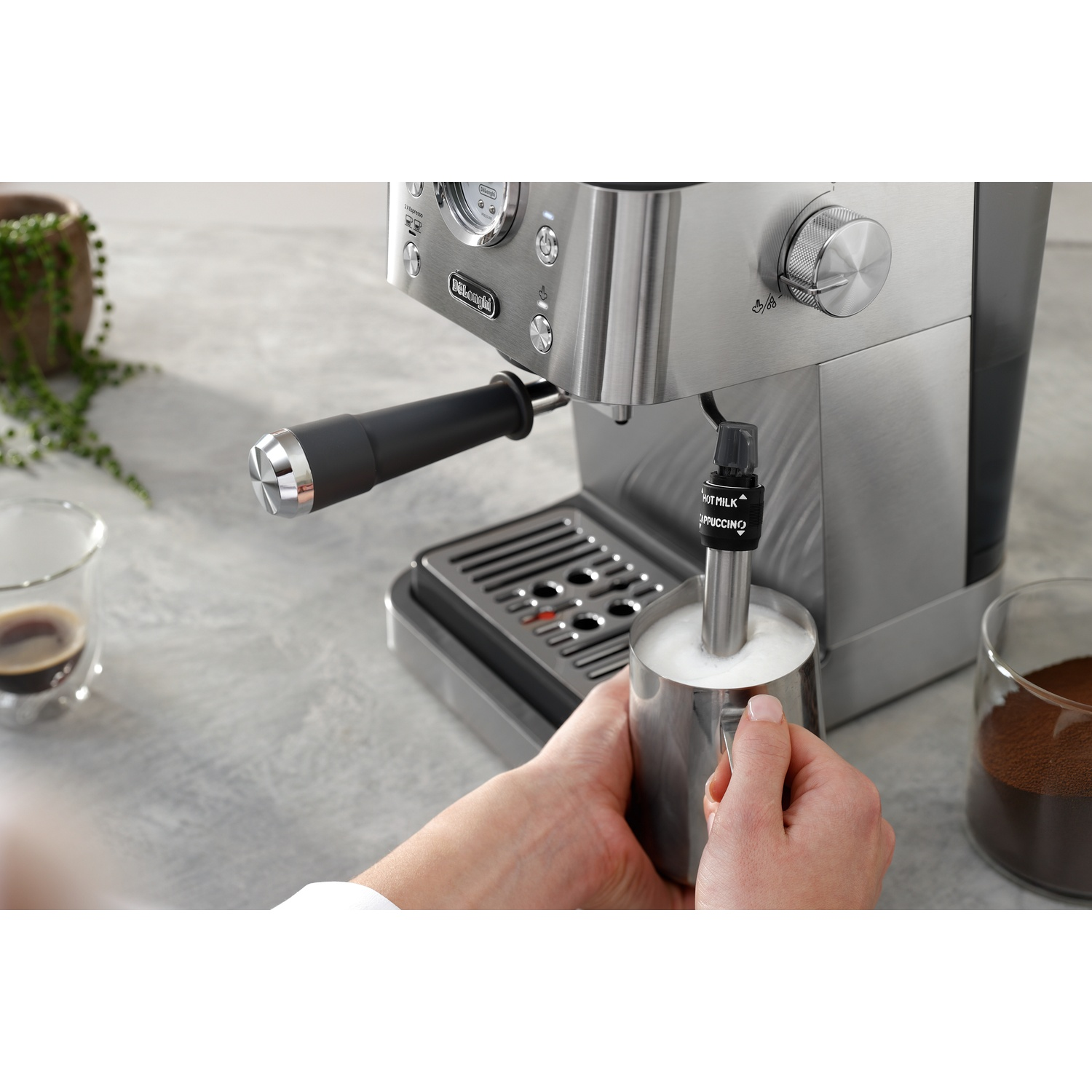 A person froths milk in a metal pitcher with an espresso machine.