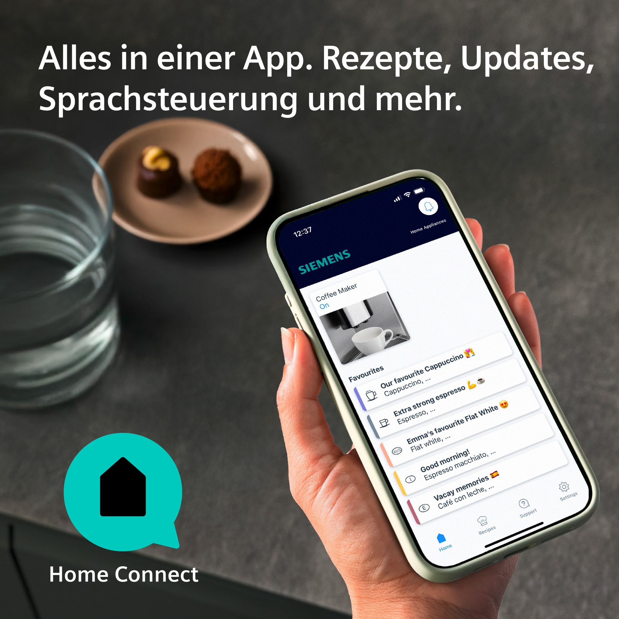 Eine Hand hält ein Smartphone mit der Home Connect App. Im Hintergrund sind ein Glas Wasser und Pralinen.
