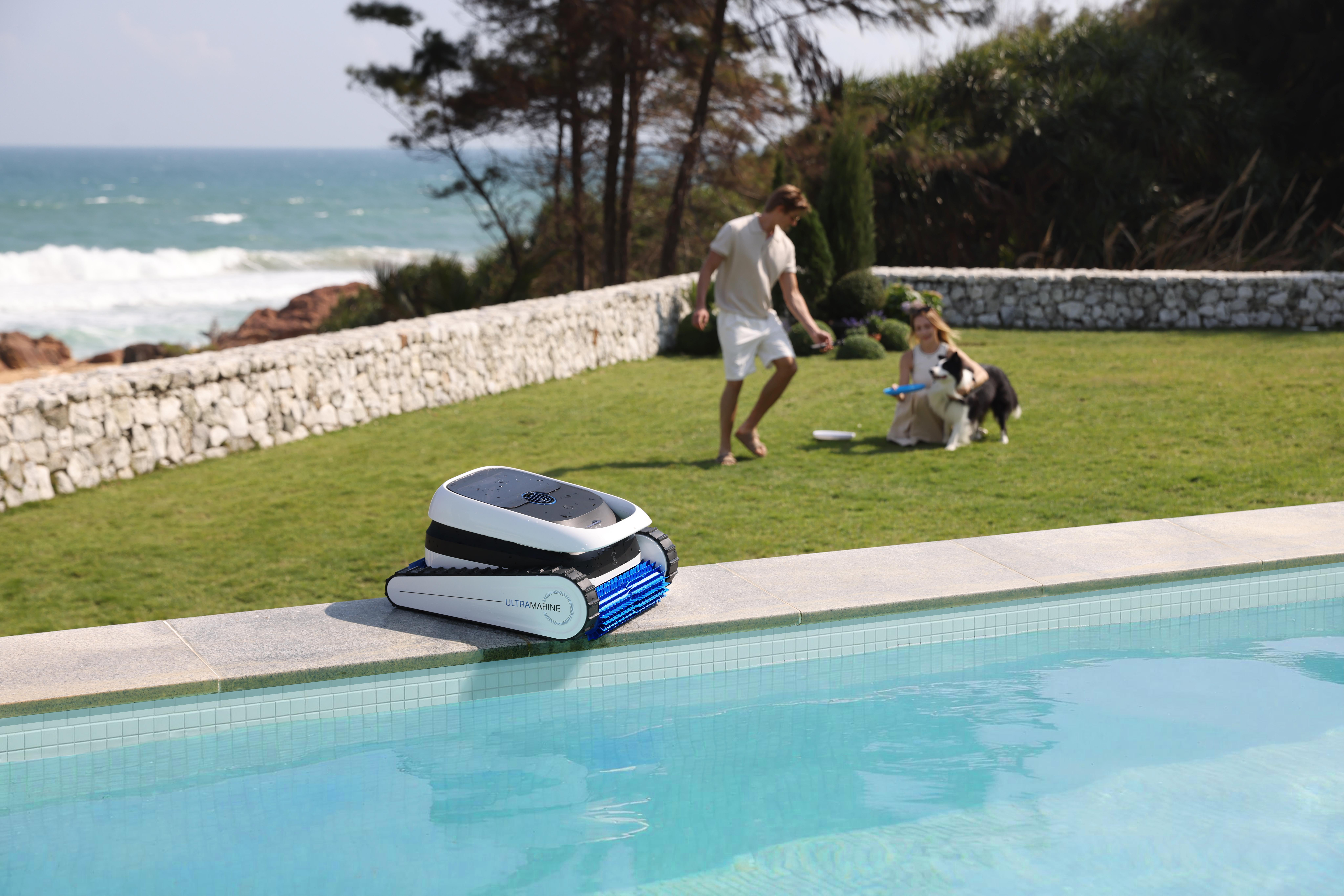 Ein Poolroboter steht am Beckenrand, im Hintergrund spielen Menschen und ein Hund.