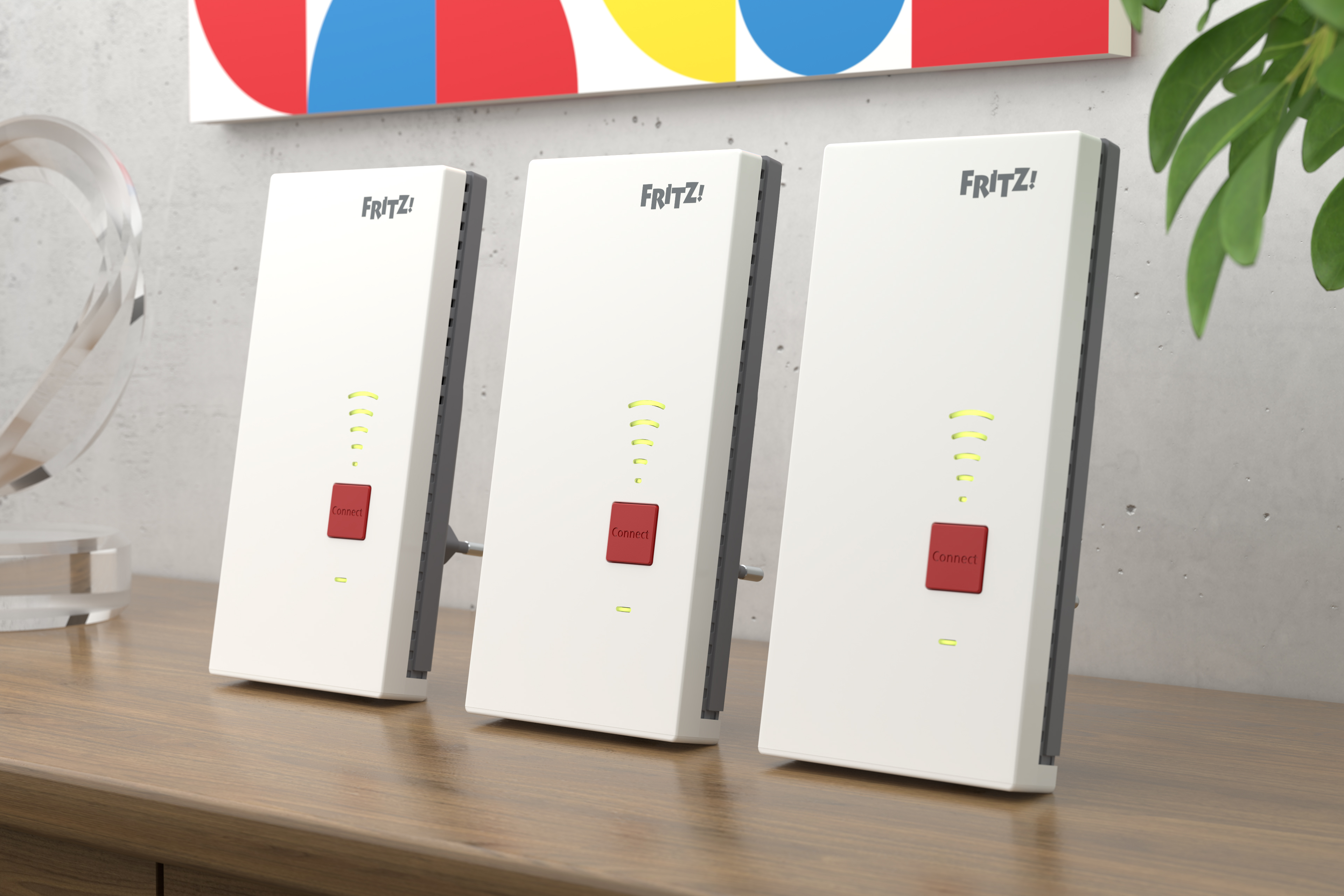Drei weiße FRITZ!Box-Router mit roten Connect-Knöpfen stehen auf einem Holztisch.