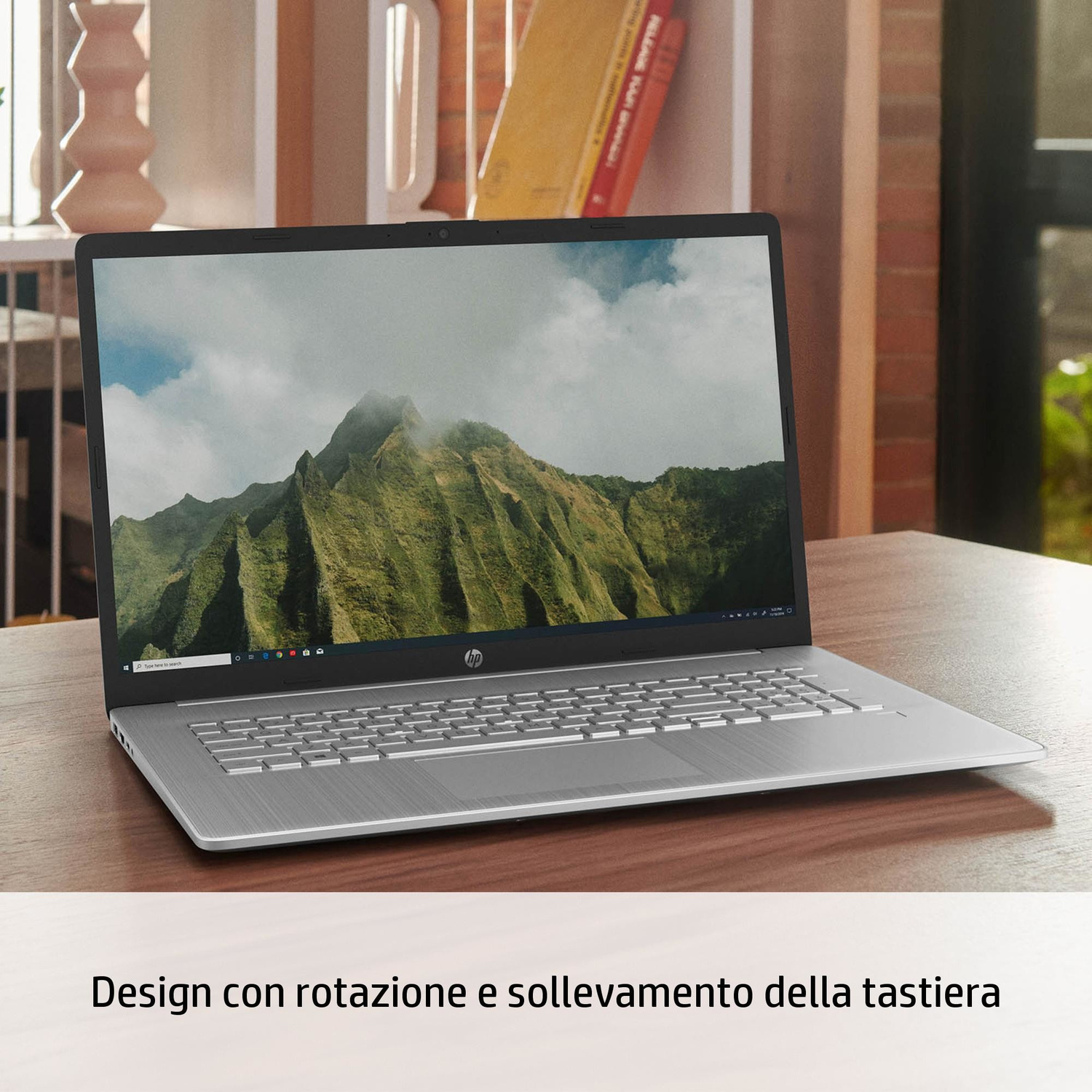 Un laptop argentato mostra uno sfondo di cima montuosa su una scrivania di legno.