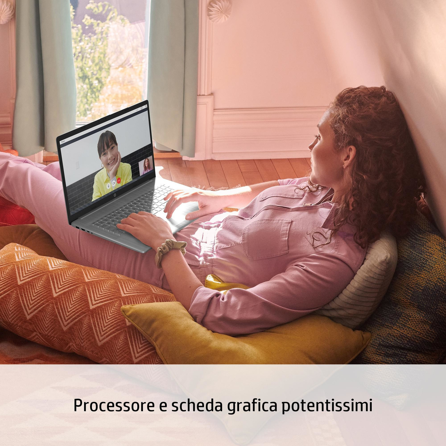 Una donna sdraiata sui cuscini usa un laptop che mostra una videochiamata.