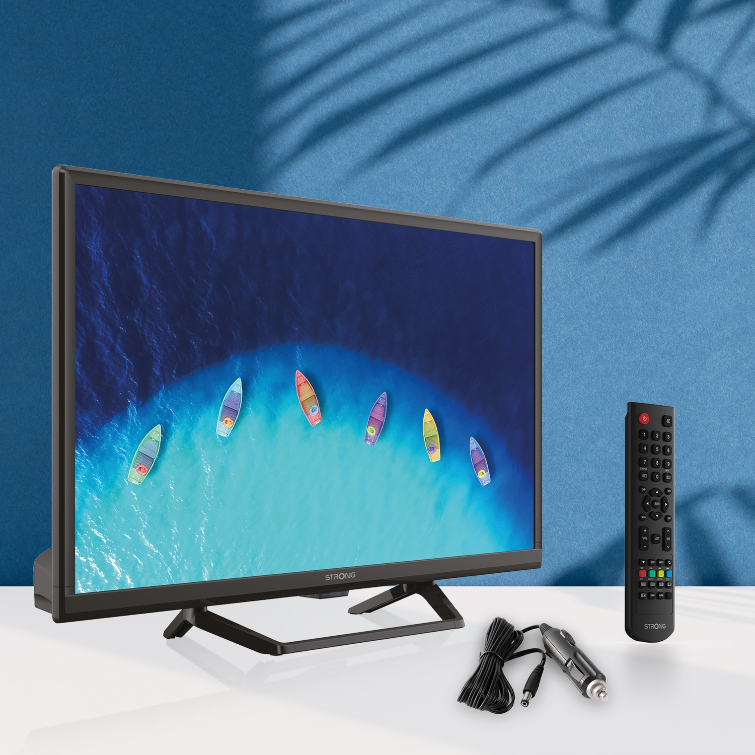 Un televisore con un'immagine di barche sul mare, con telecomando e caricabatterie per auto nelle vicinanze.