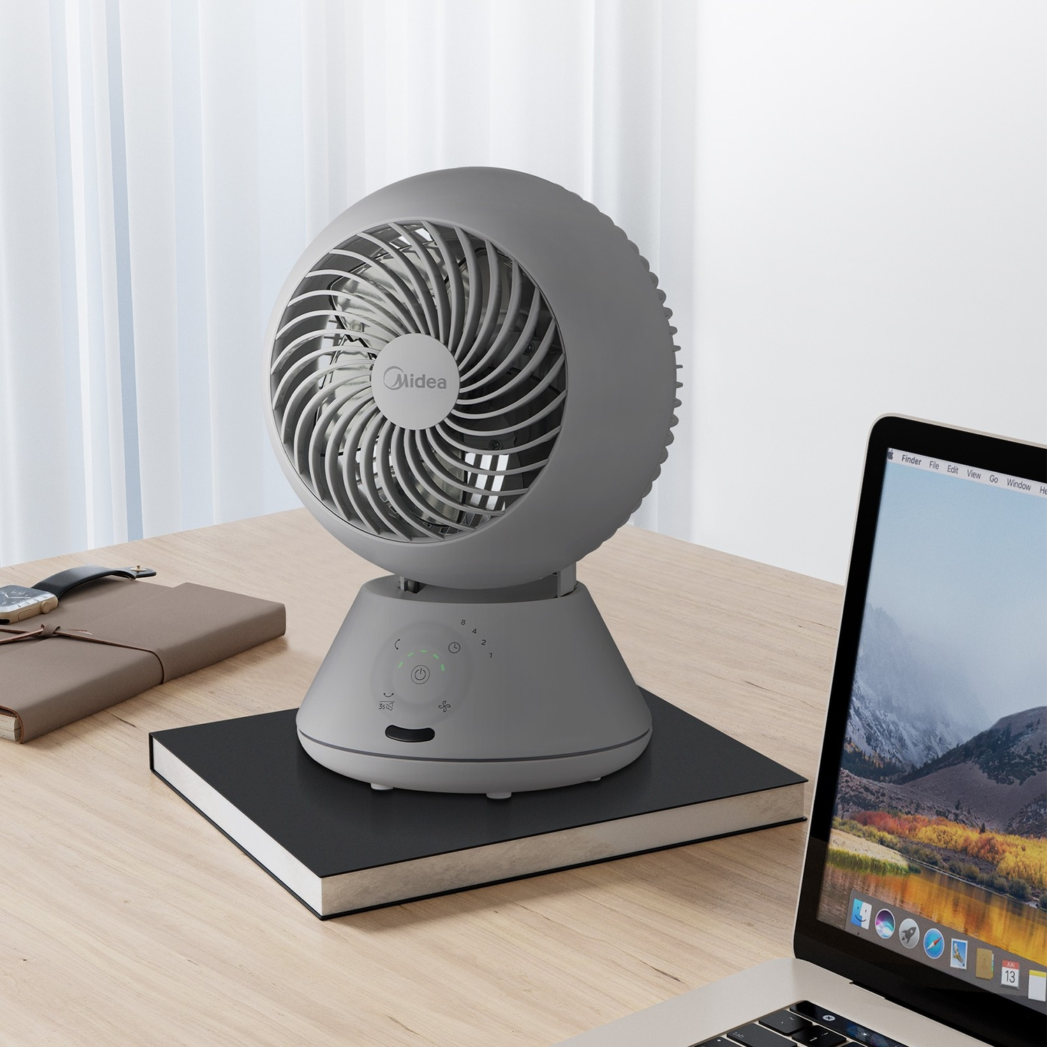 Un ventilatore da tavolo grigio su una scrivania di legno accanto a un laptop e quaderni.