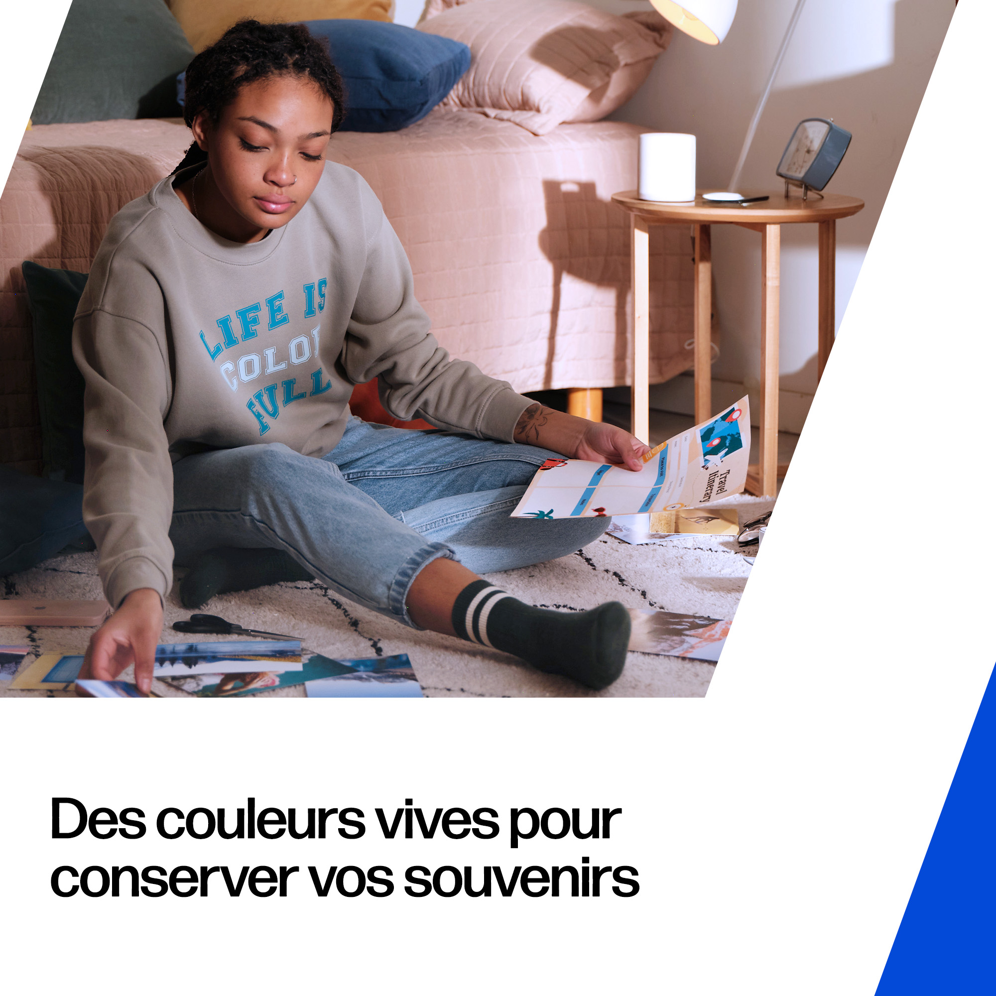 Jeune femme assise par terre avec des photos, lit et table de nuit derrière.