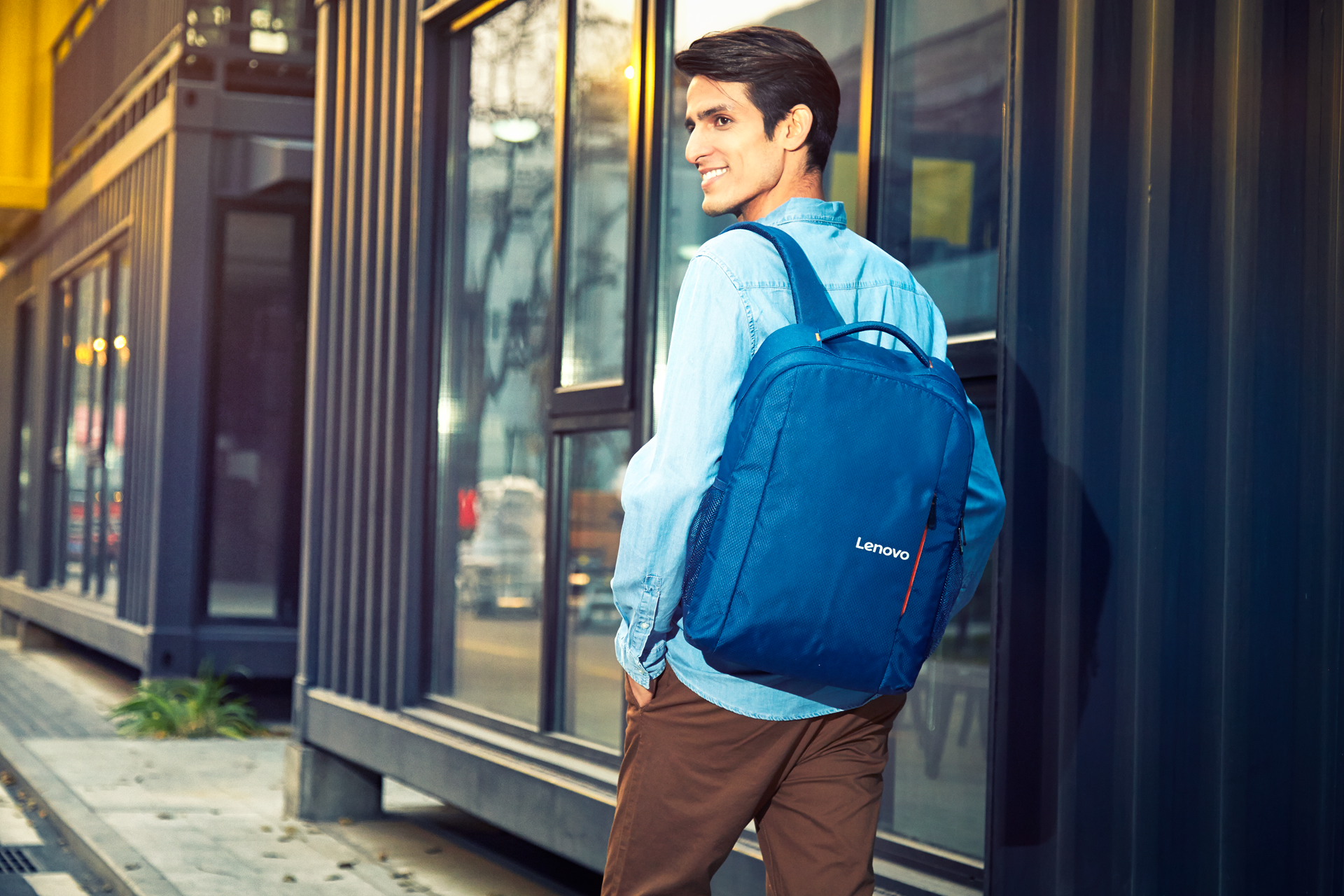 Un hombre con mochila azul y camisa de mezclilla pasa junto a ventanas.