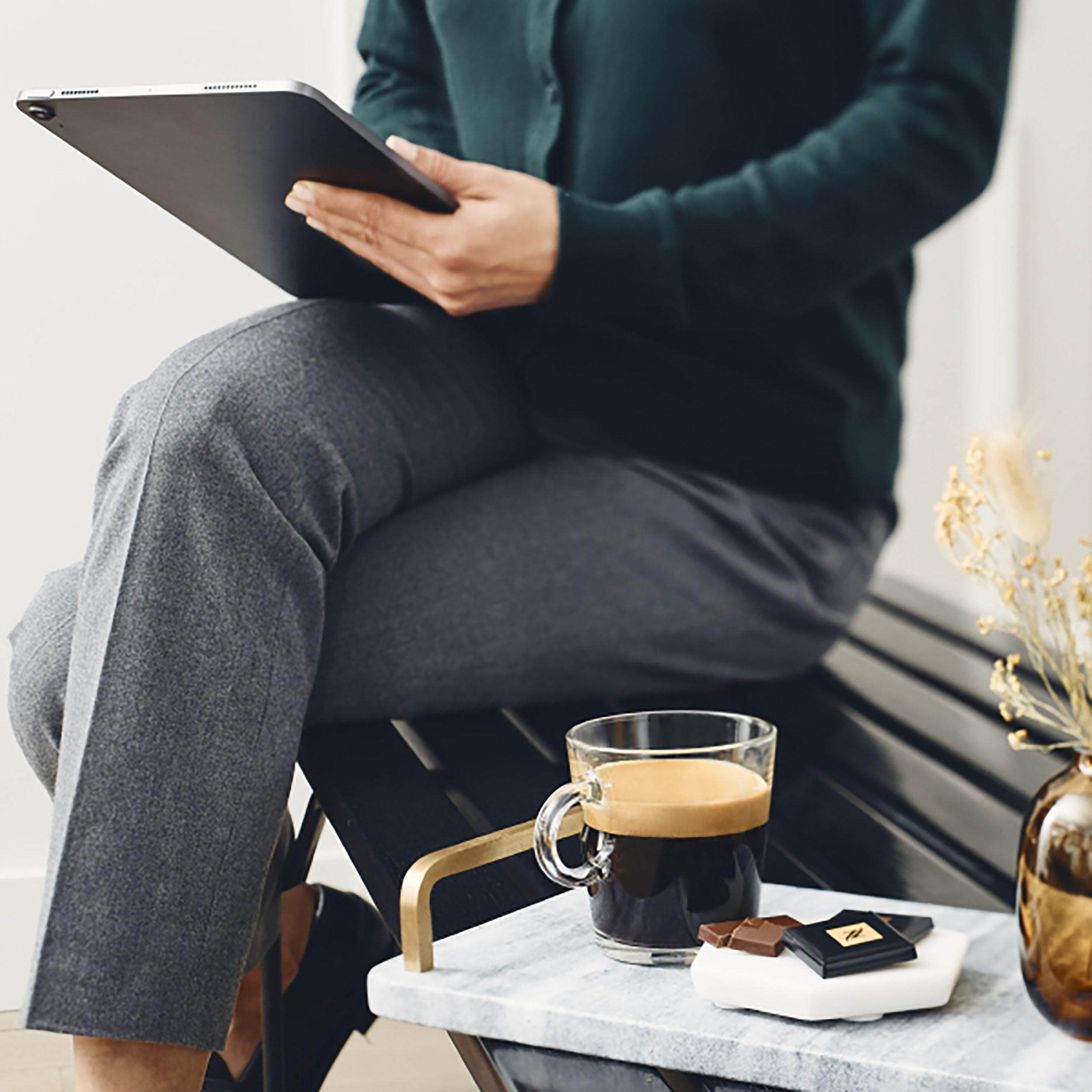 Eine Person sitzt mit einem Tablet und genießt Kaffee und Schokolade.