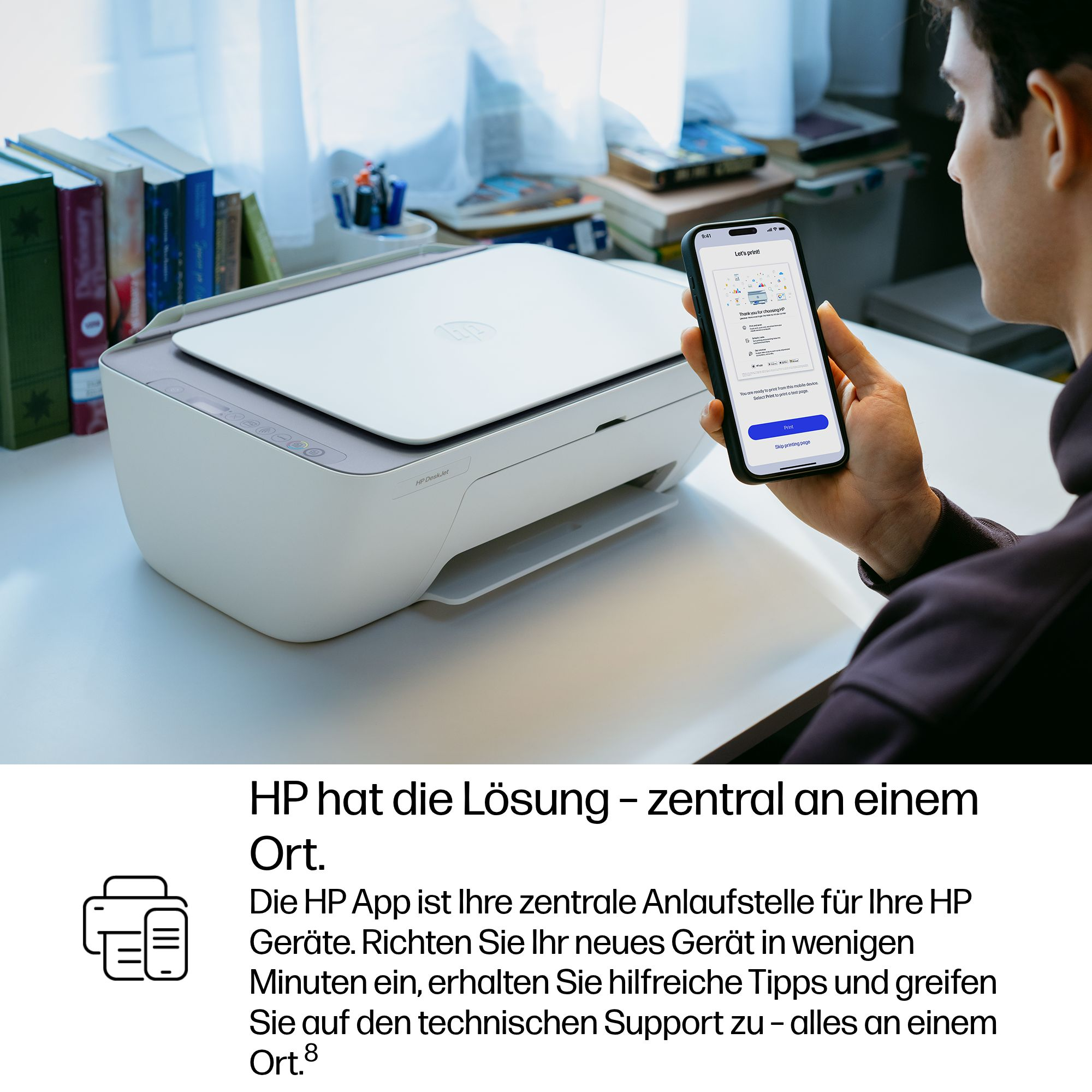 Mann hält Smartphone vor Drucker. Bucher im Regal.