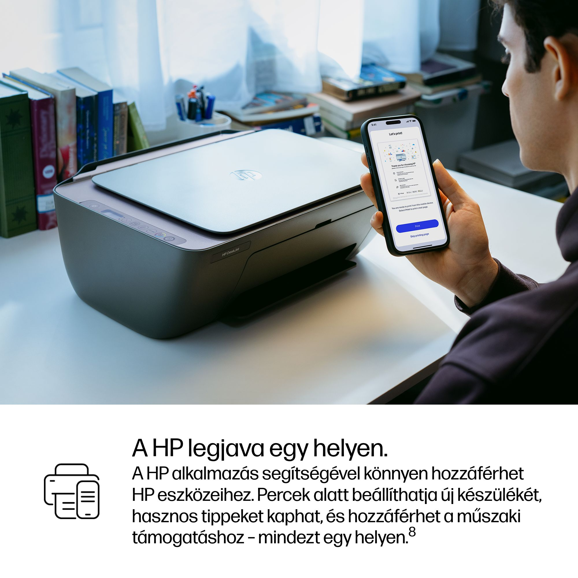 Egy férfi okostelefont tart egy HP nyomtató előtt. Könyvek a háttérben.