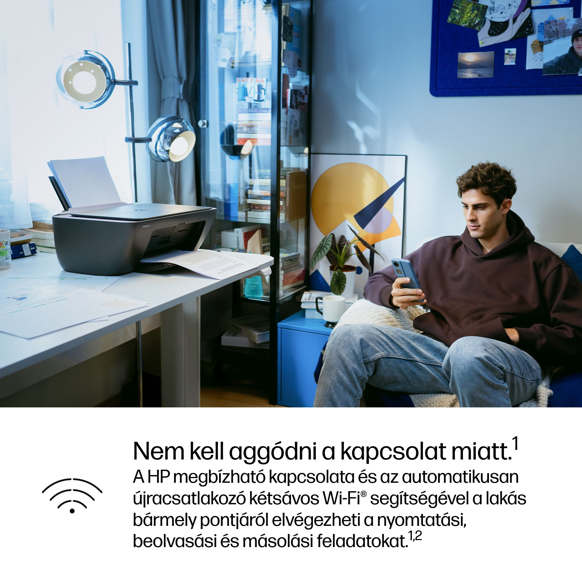 Egy férfi ül a kanapén, telefonját nézi, egy nyomtató mellett.