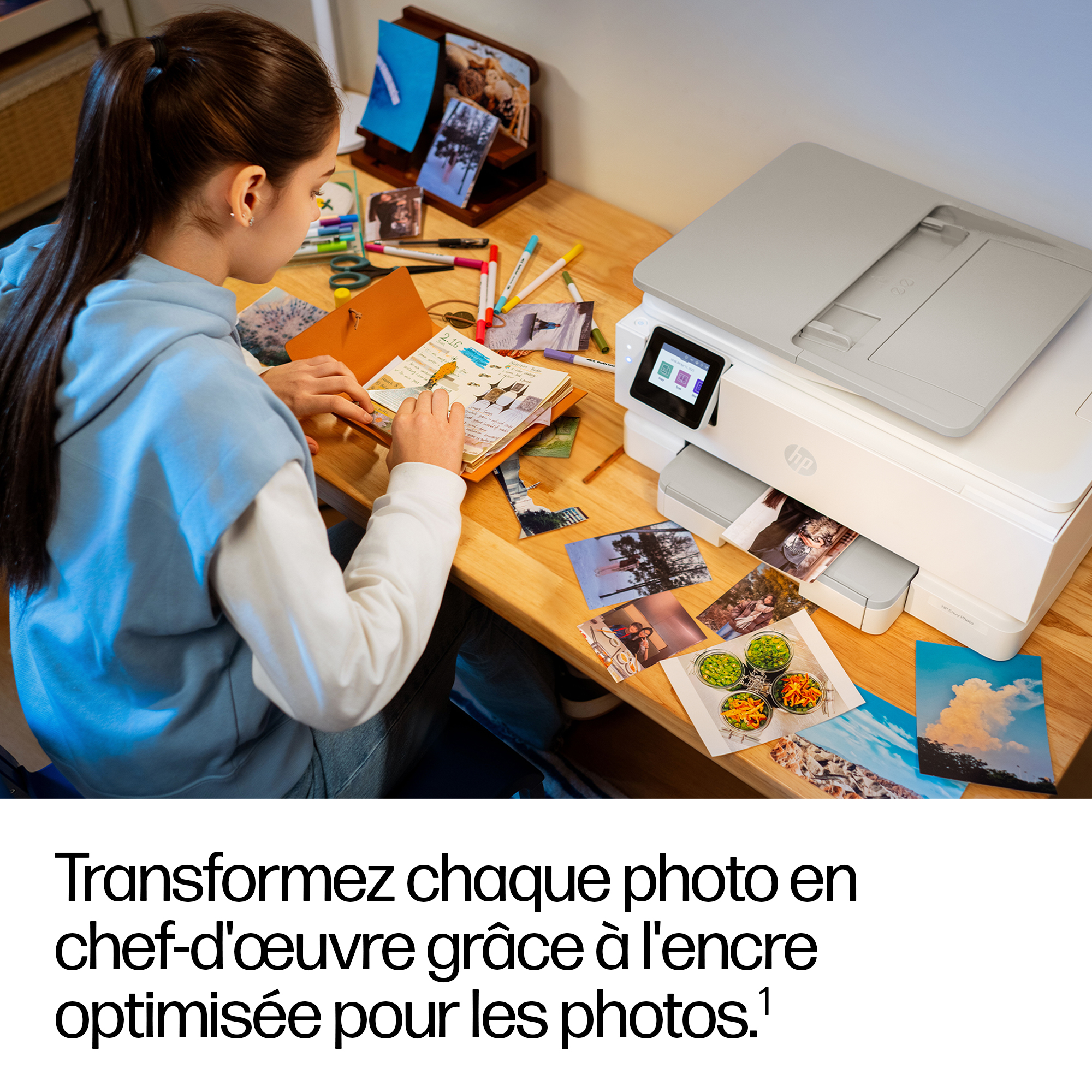 Une fille décore un journal à côté d'une imprimante, des photos sur la table.