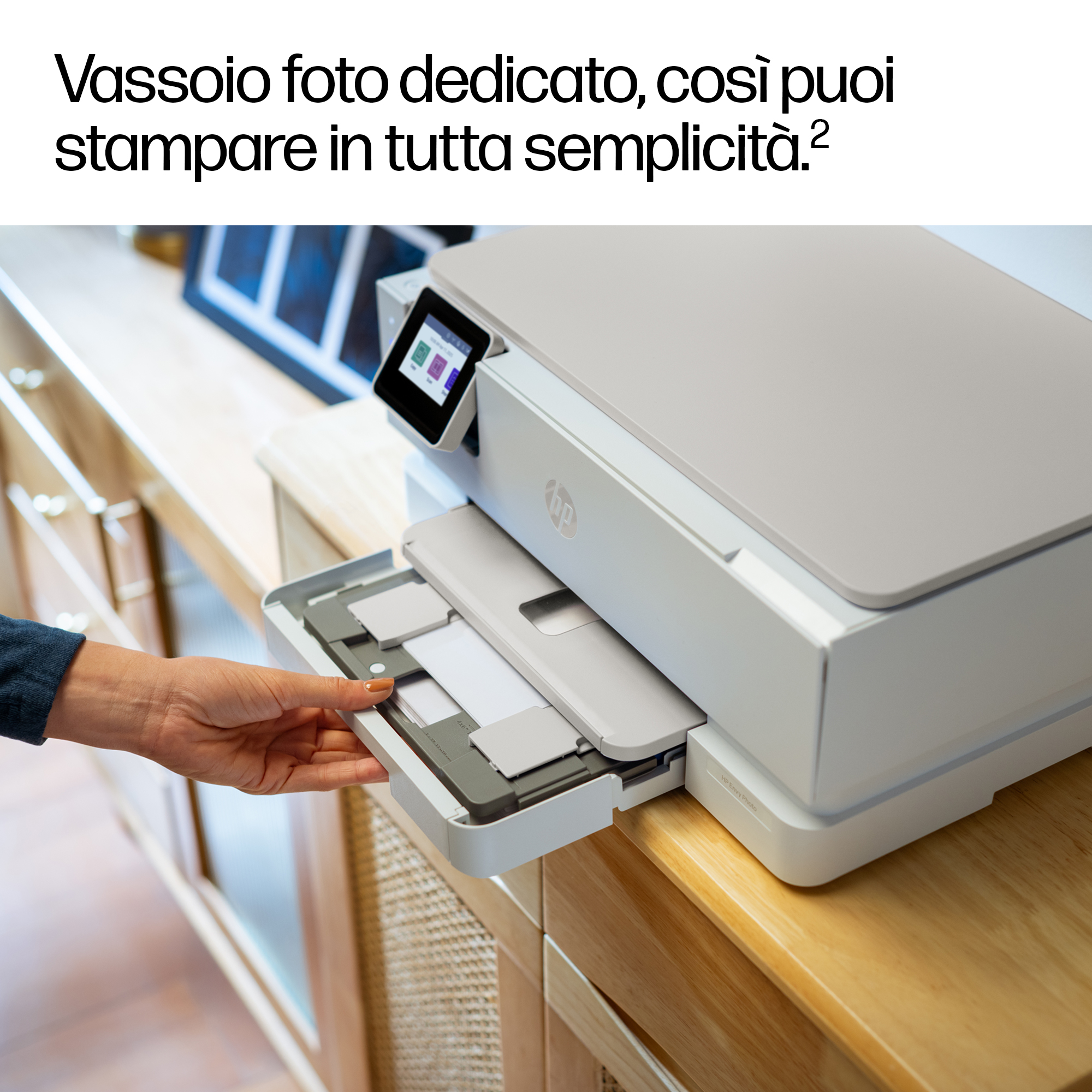 Una mano estrae un vassoio carta da una stampante HP grigio chiaro su un mobile in legno.