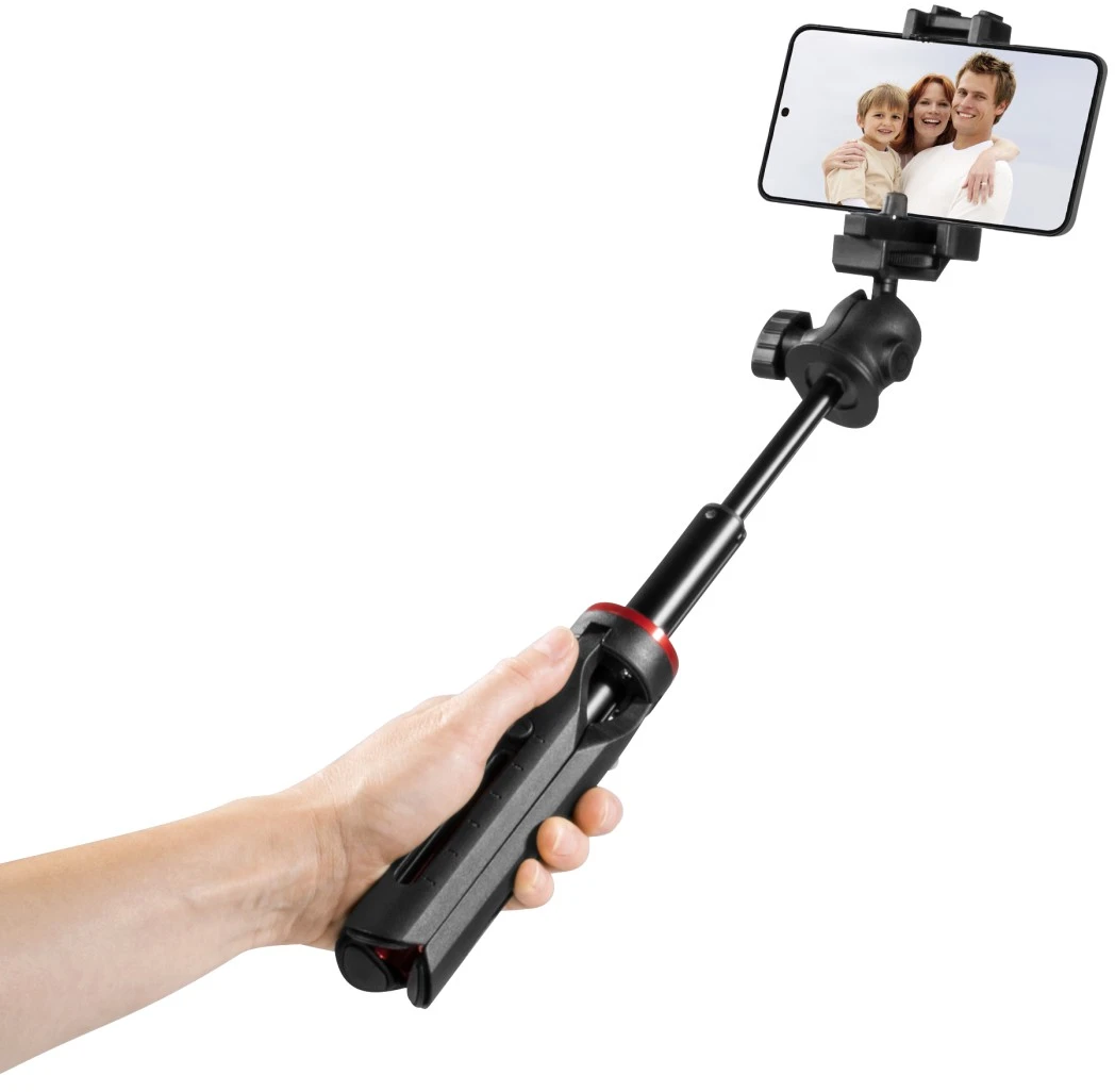 Une main tient une perche à selfie noire avec un téléphone affichant une photo de famille.
