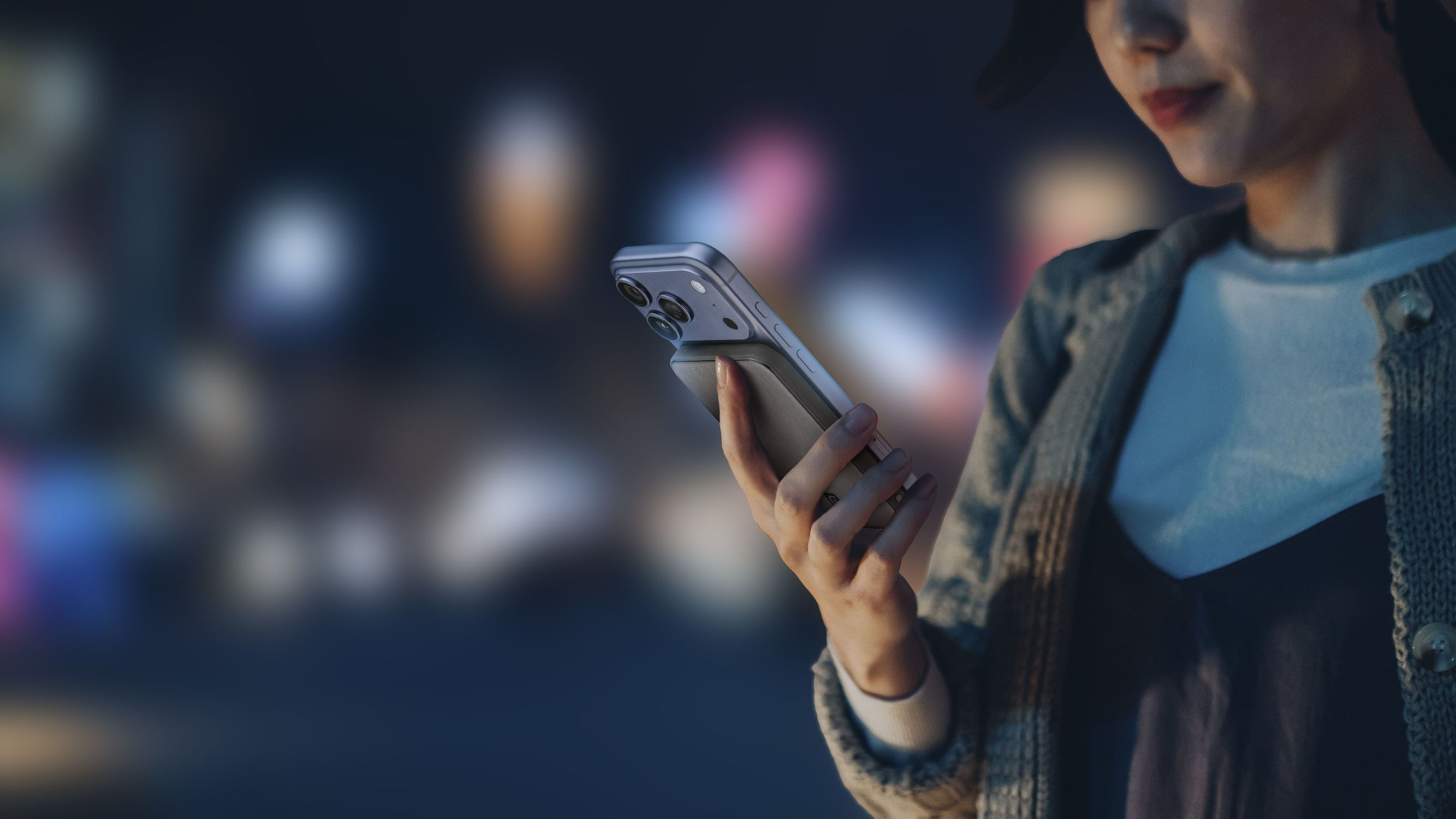 Una mujer sostiene un teléfono inteligente con cámara sobre un fondo borroso de luces.