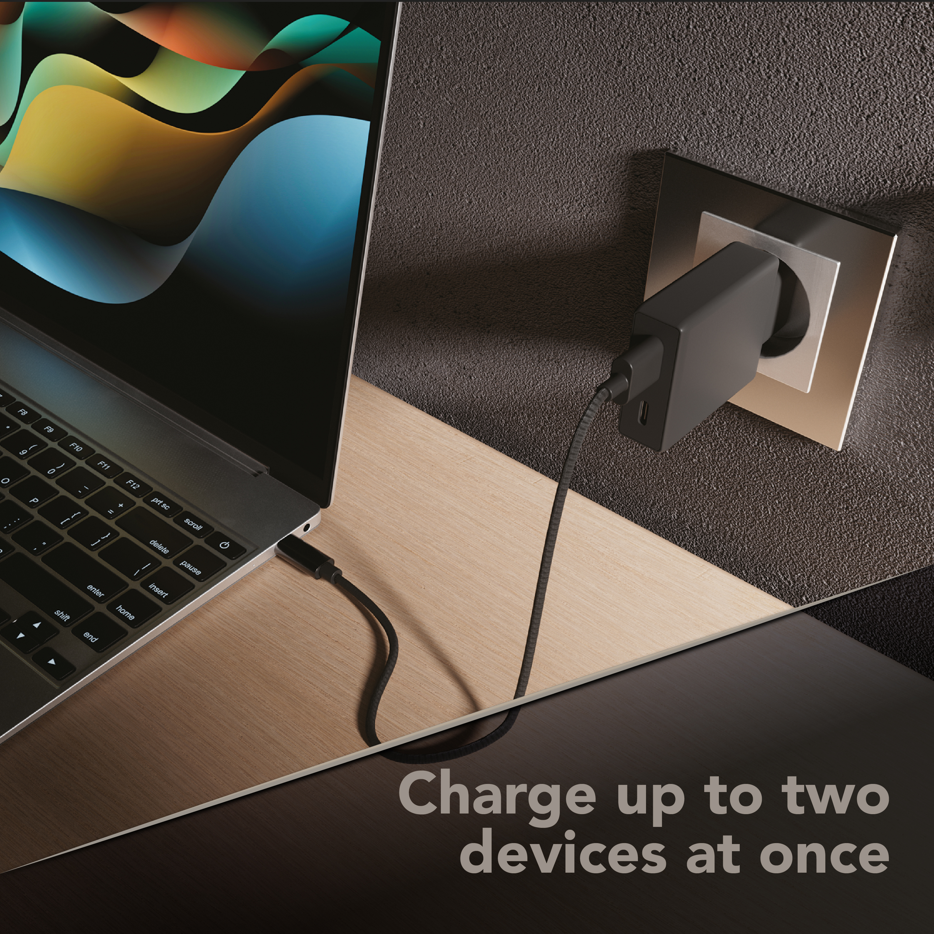 Cargador CellularLine enchufado cargando portátil, texto “Charge up to two devices at once”.
