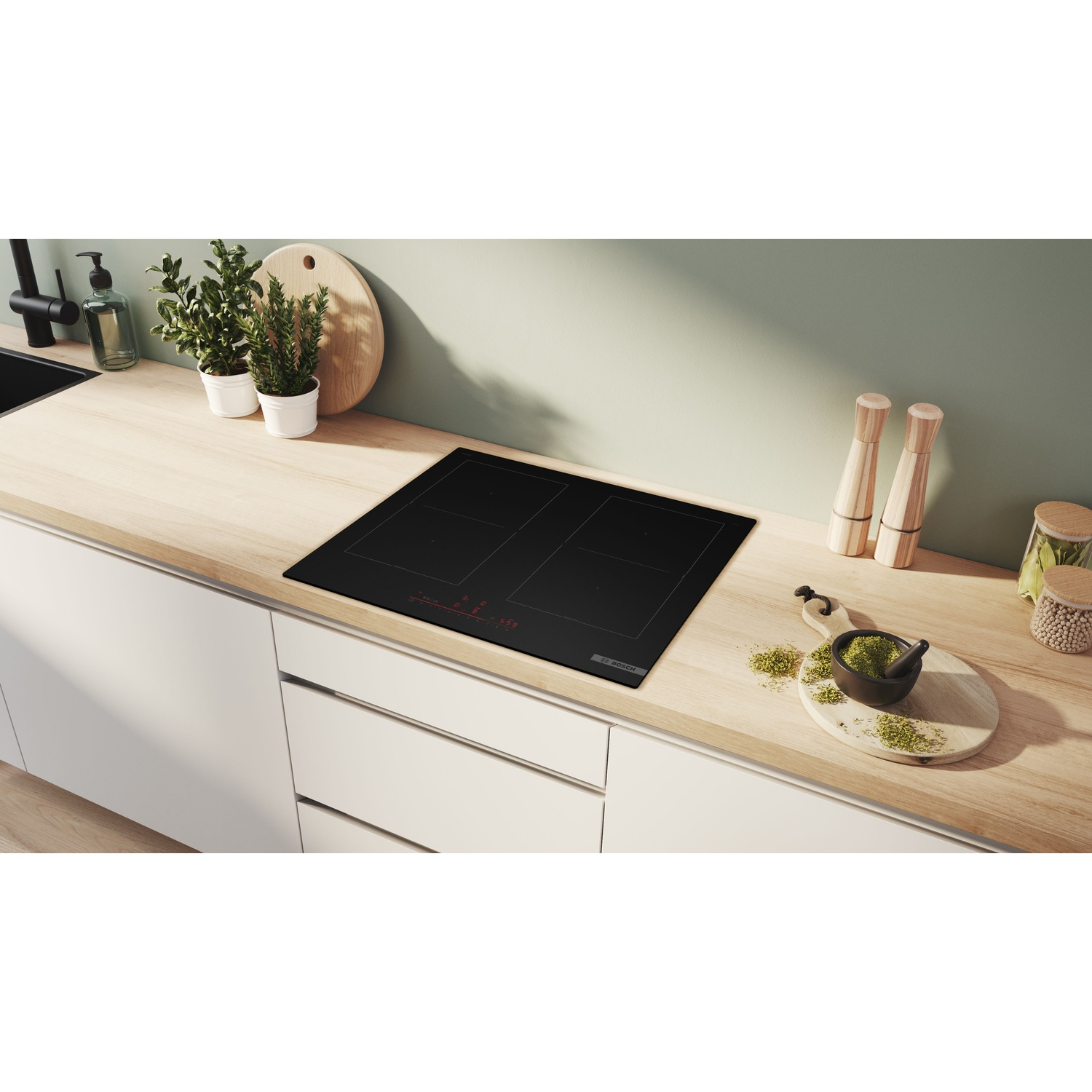 Un moderno piano cottura a induzione nero su un piano di lavoro in legno con oggetti da cucina.