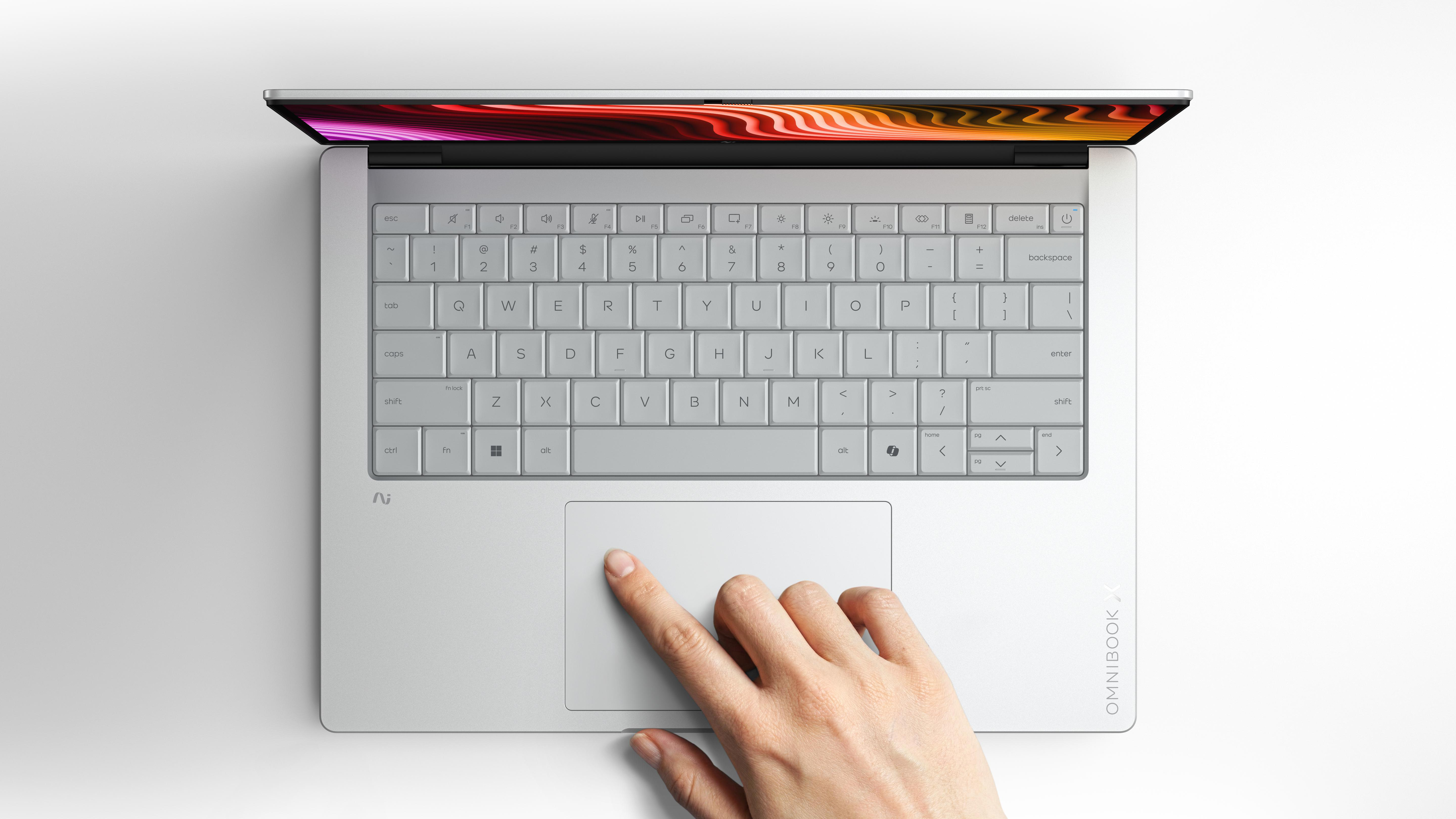 Eine Hand berührt das Touchpad eines silbernen Laptops mit beleuchtetem Bildschirm.