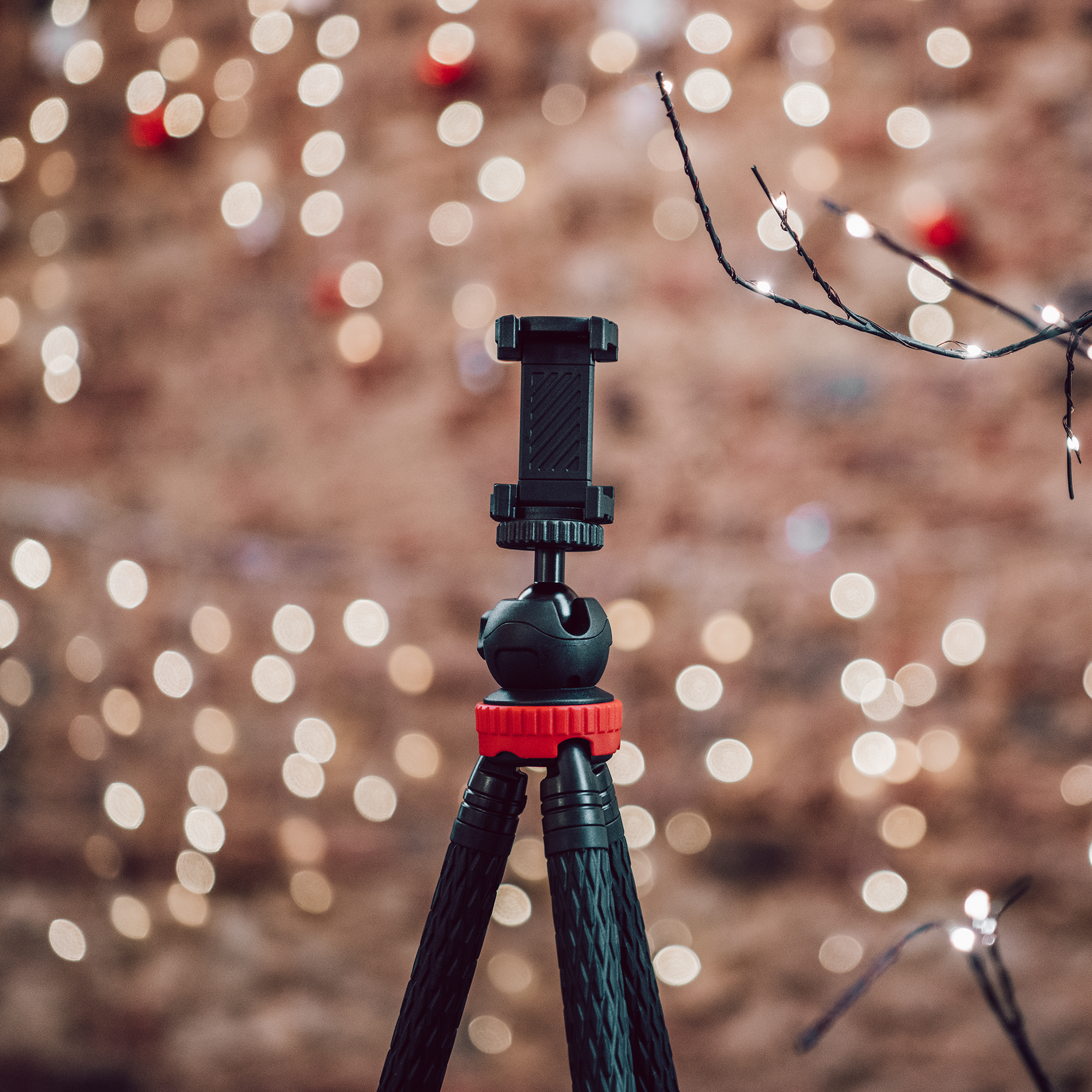 Kırmızı vurgulu siyah bir tripod, sıcak ışıkların bokeh arka planına karşı duruyor.