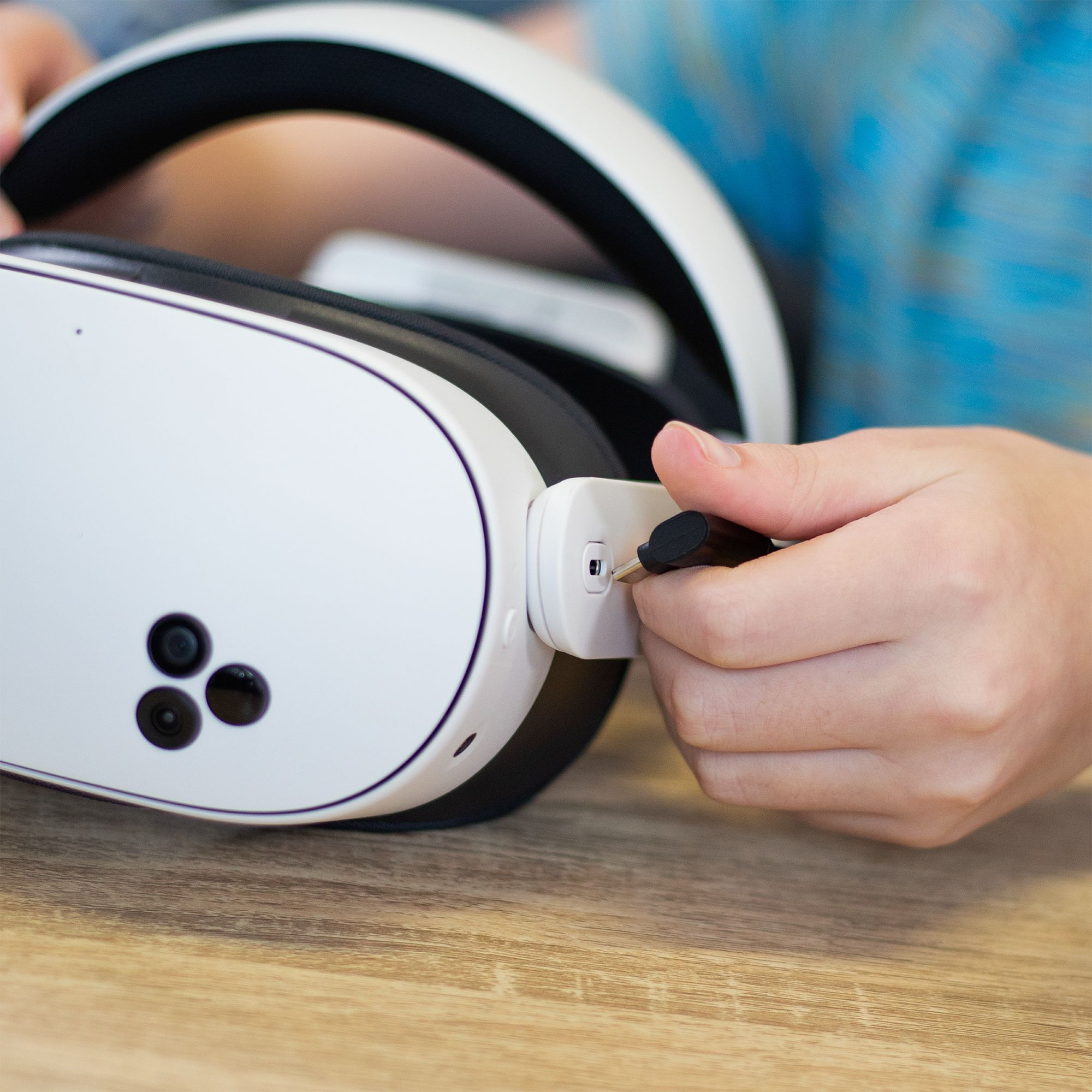 Eine Hand steckt ein schwarzes Kabel in ein weißes VR-Headset.
