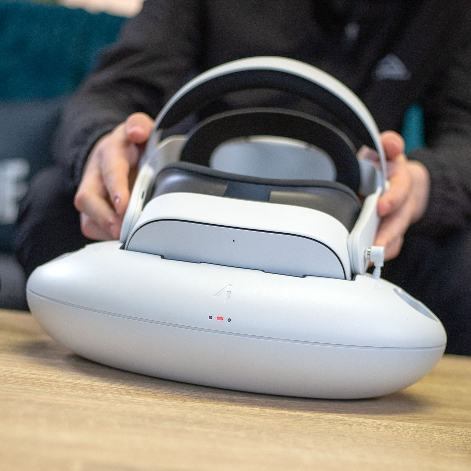 Eine weiße VR-Brille wird von Händen gehalten, die sie in ein Ladegehäuse legen.
