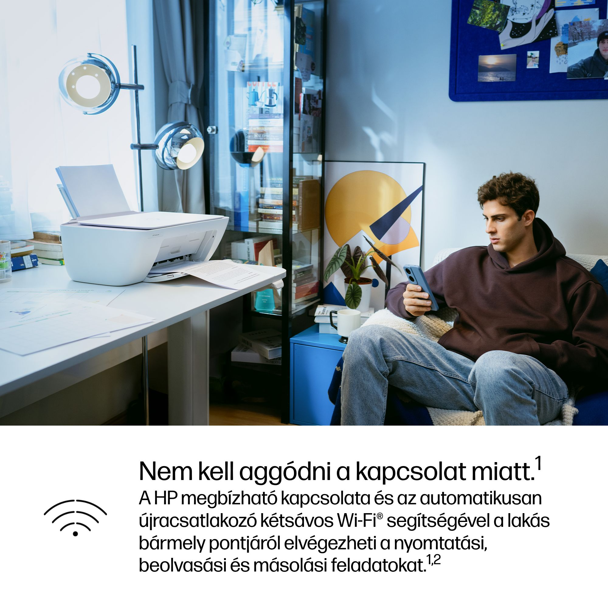 Férfi ül kanapén telefonnal, nyomtató a háttérben.