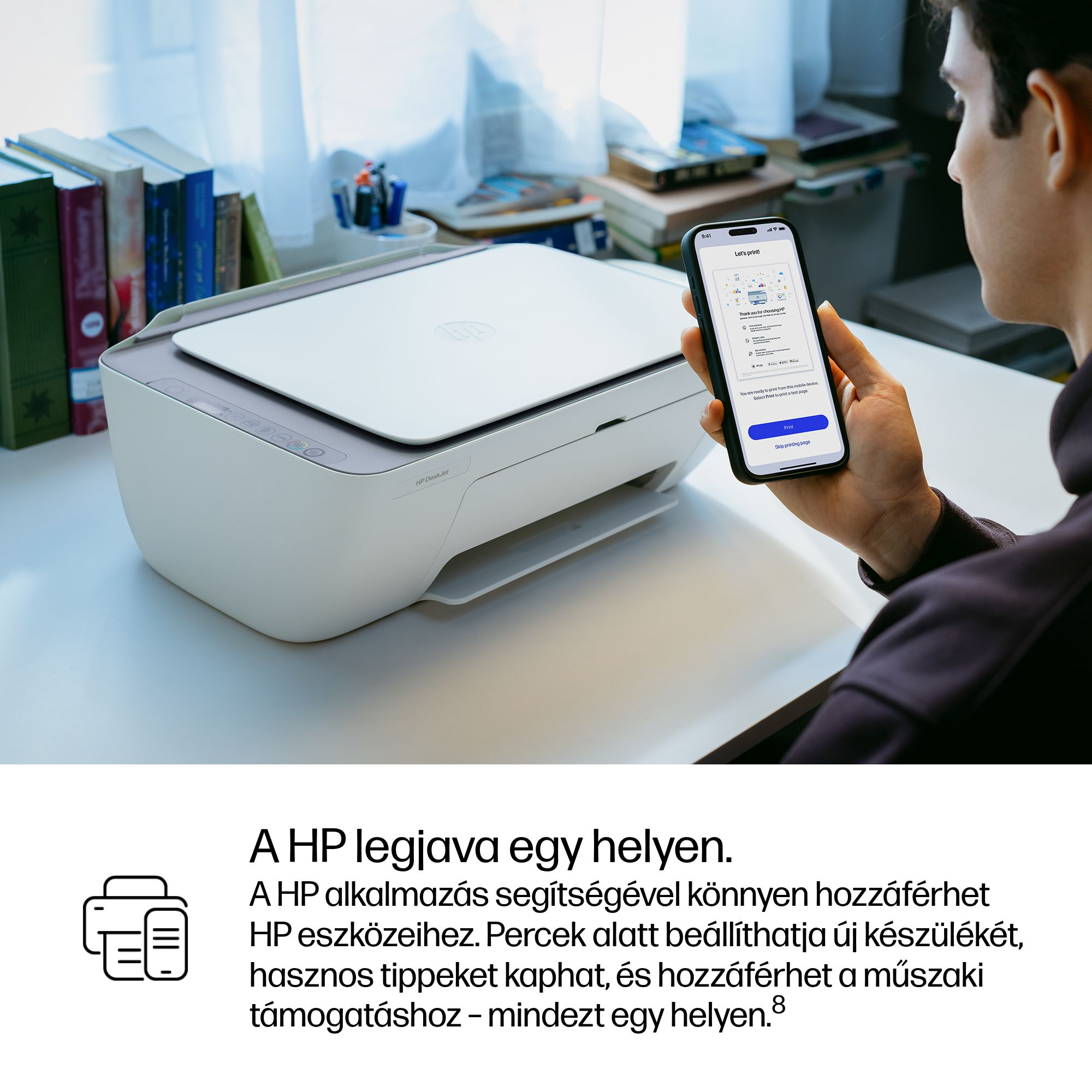 Férfi okostelefont tart HP nyomtató előtt. Könyvespolc a háttérben.